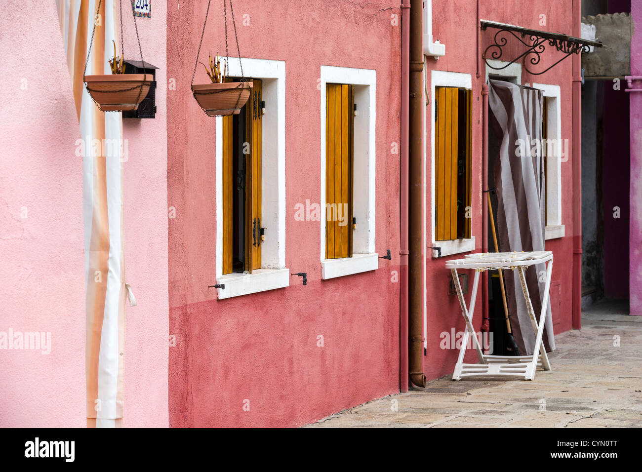 Una casa a Burano nel tipico stile con pareti dipinte di diverse tonalità di rosa e uno stendino appena al di fuori della porta Foto Stock