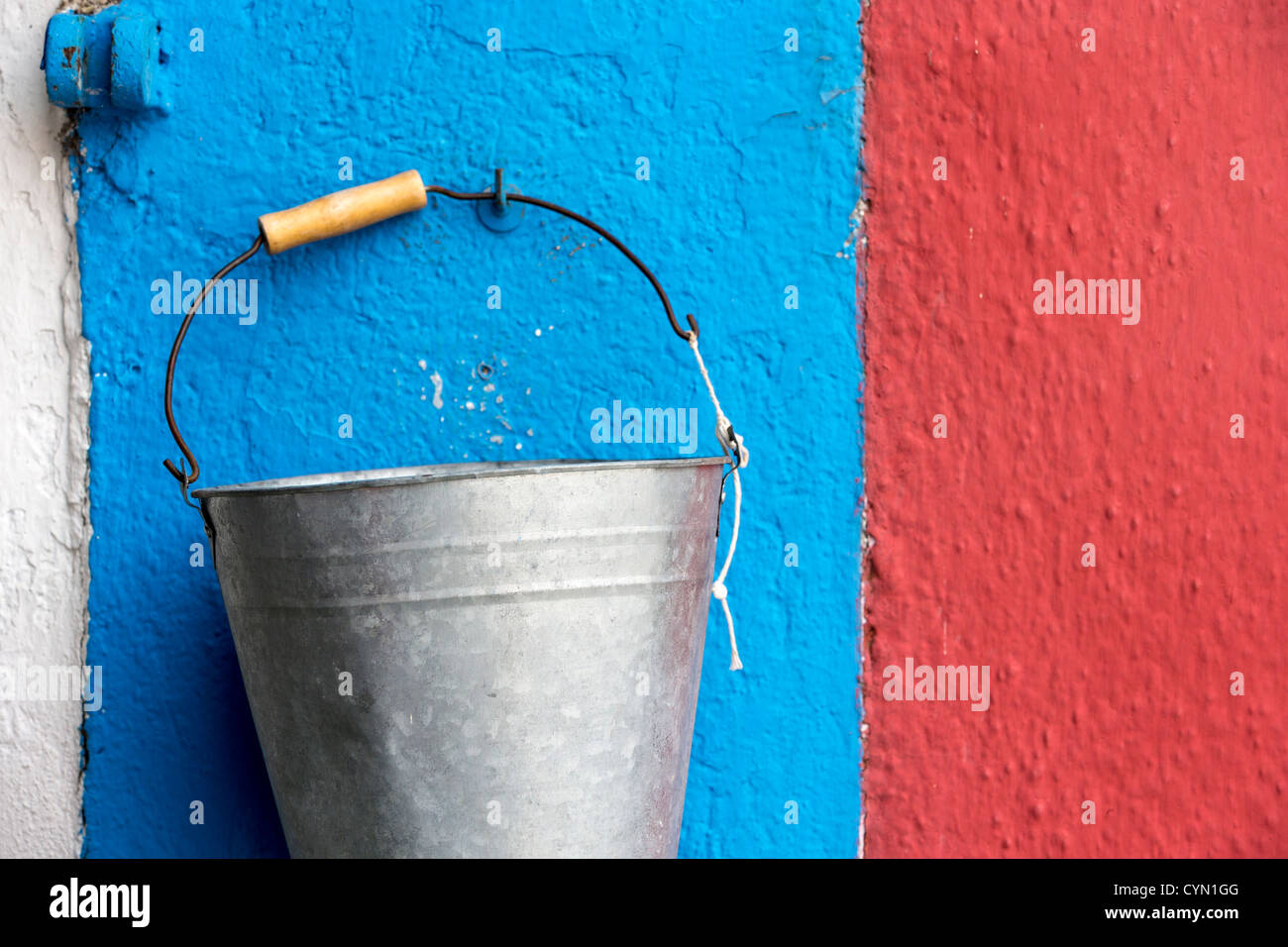 Un acciaio zincato benna appeso a una parete dipinta di rosso, bianco e blu a Burano, Venezia Foto Stock