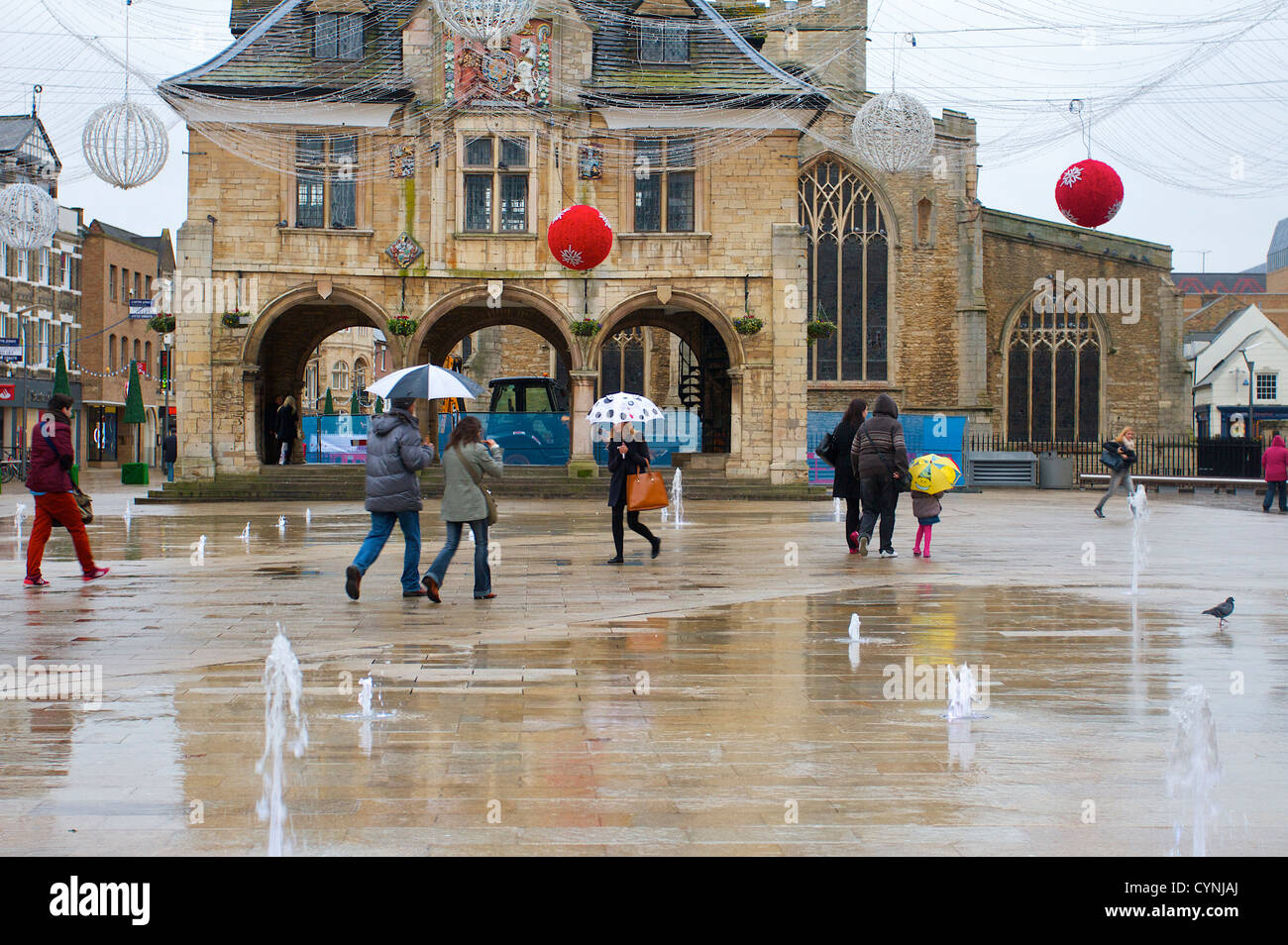 Peterborough city centre, la gente a piedi attraverso la fontana e le luci di Natale, giorno piovoso, Peterborough, Regno Unito Foto Stock