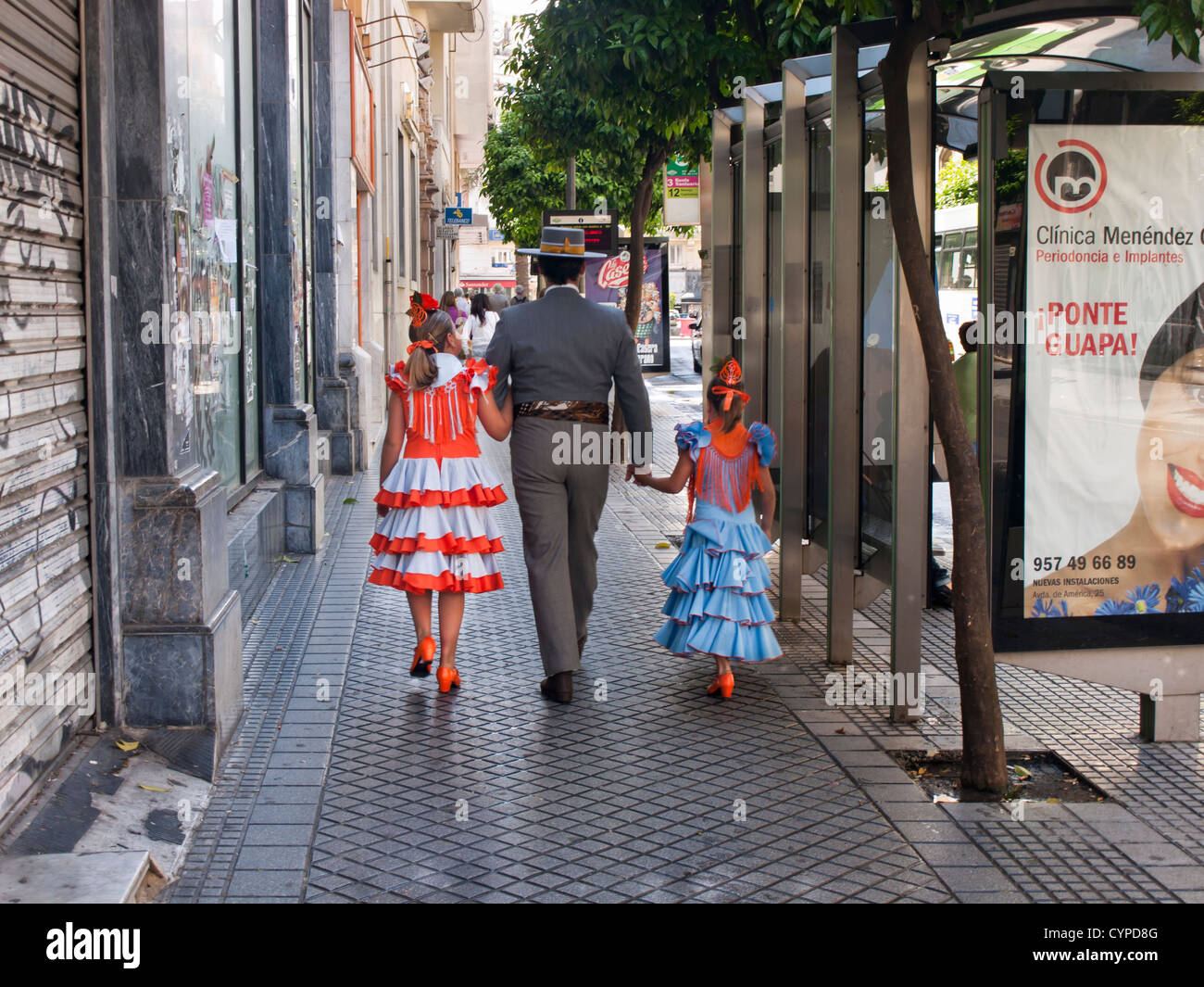 Scena di strada a Cordoba Andalusia Spagna due ragazze con il tradizionale abito flamenco,traje de flamenca con uomo a camminare Foto Stock