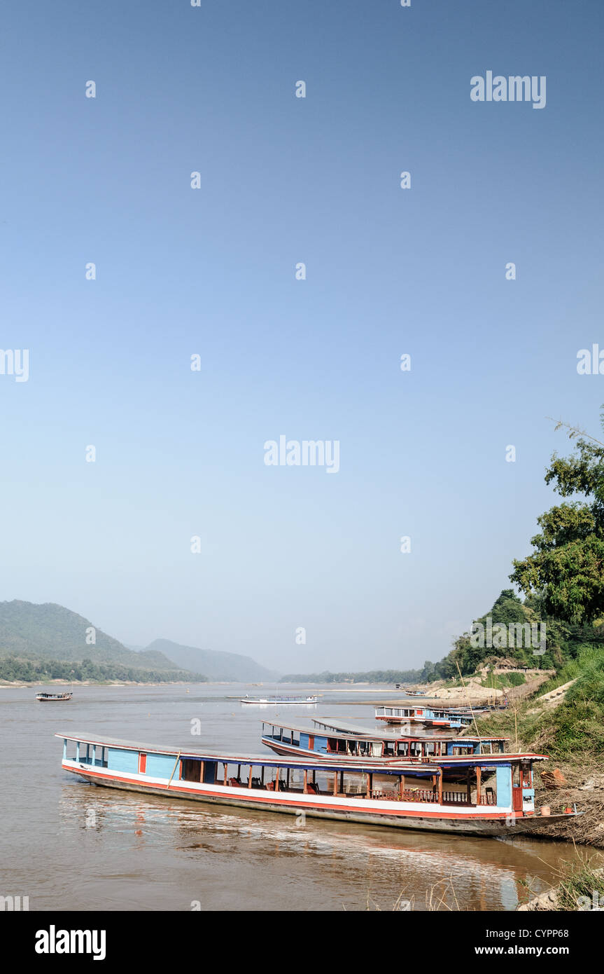 Barche a coda lunga fiume Mekong Luang Prabang Laos // LUANG PRABANG, Laos - grandi barche a coda lunga, conosciute localmente come Hua Hang Thom, sono ormeggiate lungo le rive del fiume Mekong. Queste imbarcazioni tradizionali sono dotate di alberi di trasmissione estesi e sono comunemente utilizzate per viaggi fluviali di media e lunga distanza in tutto il Laos settentrionale. Le barche includono spesso tettoie e posti a sedere per più passeggeri, che servono come taxi fluviali e traghetti locali che collegano le comunità lungo il canale. Luang Prabang, un sito patrimonio dell'umanità dell'UNESCO, si trova alla confluenza dei fiumi Mekong e Nam Khan nel nord di L Foto Stock