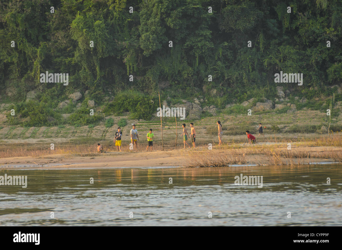I ragazzi giocano a Ball Mekong River sandbank Luang Prabang Laos // LUANG PRABANG, Laos — Un gruppo di ragazzi gioca una partita su un'isola di sabbia nel mezzo del fiume Mekong vicino a Luang Prabang nel Laos centrale. Il fiume Mekong, uno dei principali corsi d'acqua dell'Asia, scorre attraverso Luang Prabang, una città patrimonio dell'umanità dell'UNESCO conosciuta per il suo patrimonio architettonico e culturale ben conservato. Queste barre di sabbia stagionali in genere emergono durante la stagione secca quando il livello dell'acqua si ritira, creando isole temporanee utilizzate dalle comunità locali per attività ricreative e ricreative. Luang Prabang si trova alla confluenza del Mekon Foto Stock