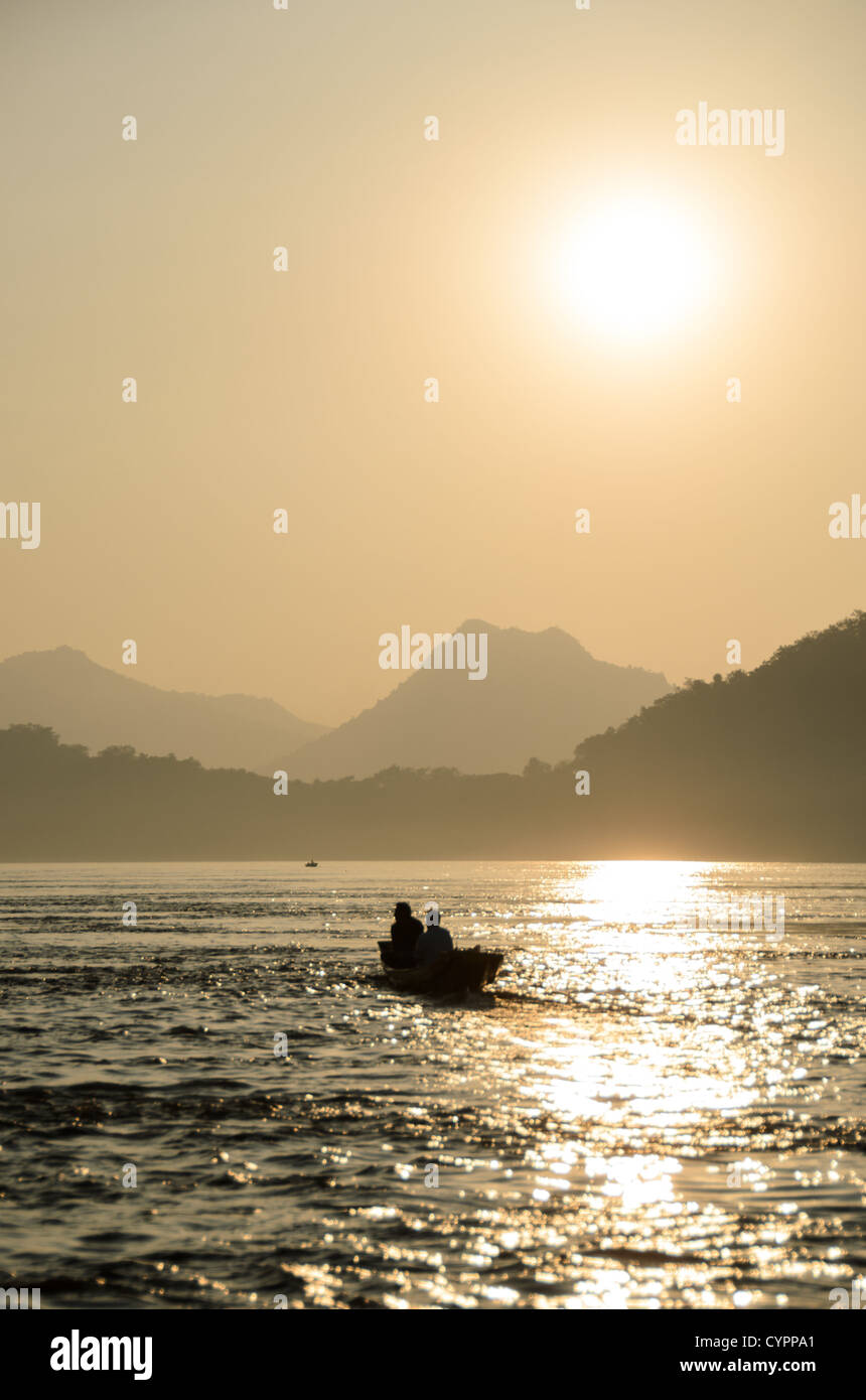 Barca a coda lunga sul fiume Mekong Luang Prabang Laos // LUANG PRABANG, Laos - due uomini navigano su una tradizionale barca a coda lunga sul fiume Mekong nel tardo pomeriggio mentre si dirigono verso il tramonto vicino a Luang Prabang. Il fiume Mekong funge da vitale via di trasporto per le comunità di tutto il Laos, che scorre per oltre 4.350 chilometri dall'altopiano tibetano al Mar Cinese meridionale. Le barche a coda lunga sono comunemente utilizzate lungo il fiume sia per il trasporto che per la pesca da parte dei residenti locali. Luang Prabang, patrimonio dell'umanità dell'UNESCO dal 1995, si trova alla confluenza del Mekong e. Foto Stock