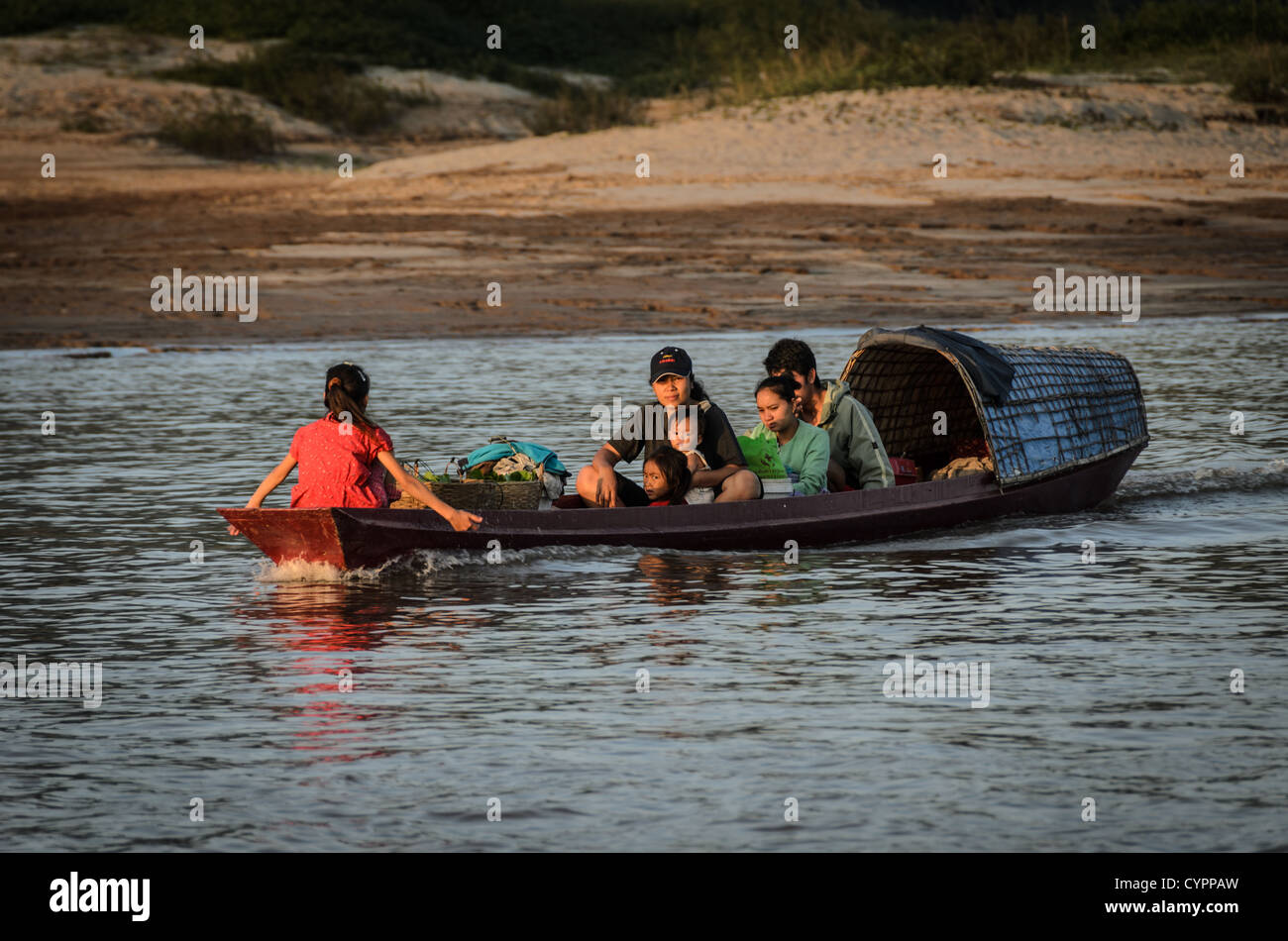 Barca a coda lunga sul fiume Mekong Luang Prabang Laos // LUANG PRABANG, Laos - Una piccola barca a coda lunga parzialmente coperta trasporta una famiglia attraverso il fiume Mekong verso il mercato di Luang Prabang. Questa tradizionale barca in legno, gestita da un barcaiolo locale, serve come mezzo di trasporto essenziale per le comunità fluviali lungo il Mekong. L'attraversamento collega le aree rurali al vivace mercato di Luang Prabang all'interno della città patrimonio dell'umanità dell'UNESCO. Luang Prabang, situata alla confluenza dei fiumi Mekong e Nam Khan, è stata dichiarata Patrimonio dell'Umanità nel 1995 per la sua ben conservata a Foto Stock