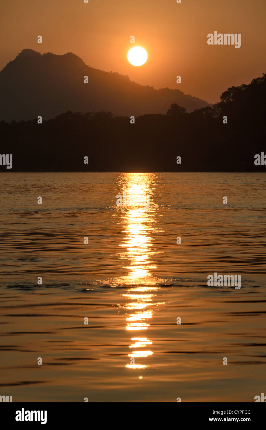 Tramonto sul fiume Mekong Luang Prabang Laos // LUANG PRABANG, Laos - il sole tramonta si riflette sulle acque ondulate del fiume Mekong vicino a Luang Prabang, con sagome di montagna visibili in lontananza. Il fiume Mekong scorre attraverso il Laos settentrionale, fungendo da canale vitale per il trasporto e il commercio nella regione. Luang Prabang, situata alla confluenza dei fiumi Mekong e Nam Khan, è un sito patrimonio dell'umanità dell'UNESCO riconosciuto per il suo patrimonio architettonico e culturale ben conservato. L'antica città servì come capitale reale del regno di Luang Prabang fino al 1975 e remai Foto Stock