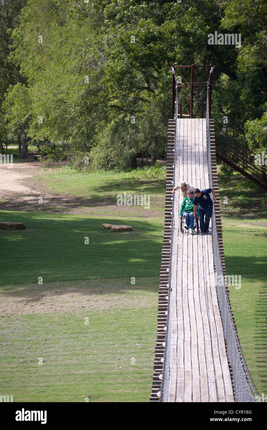 Teens push e pull amico in carrozzella tra asse di legno ponte oscillante su San Gabriel River nel Texas centrale Foto Stock