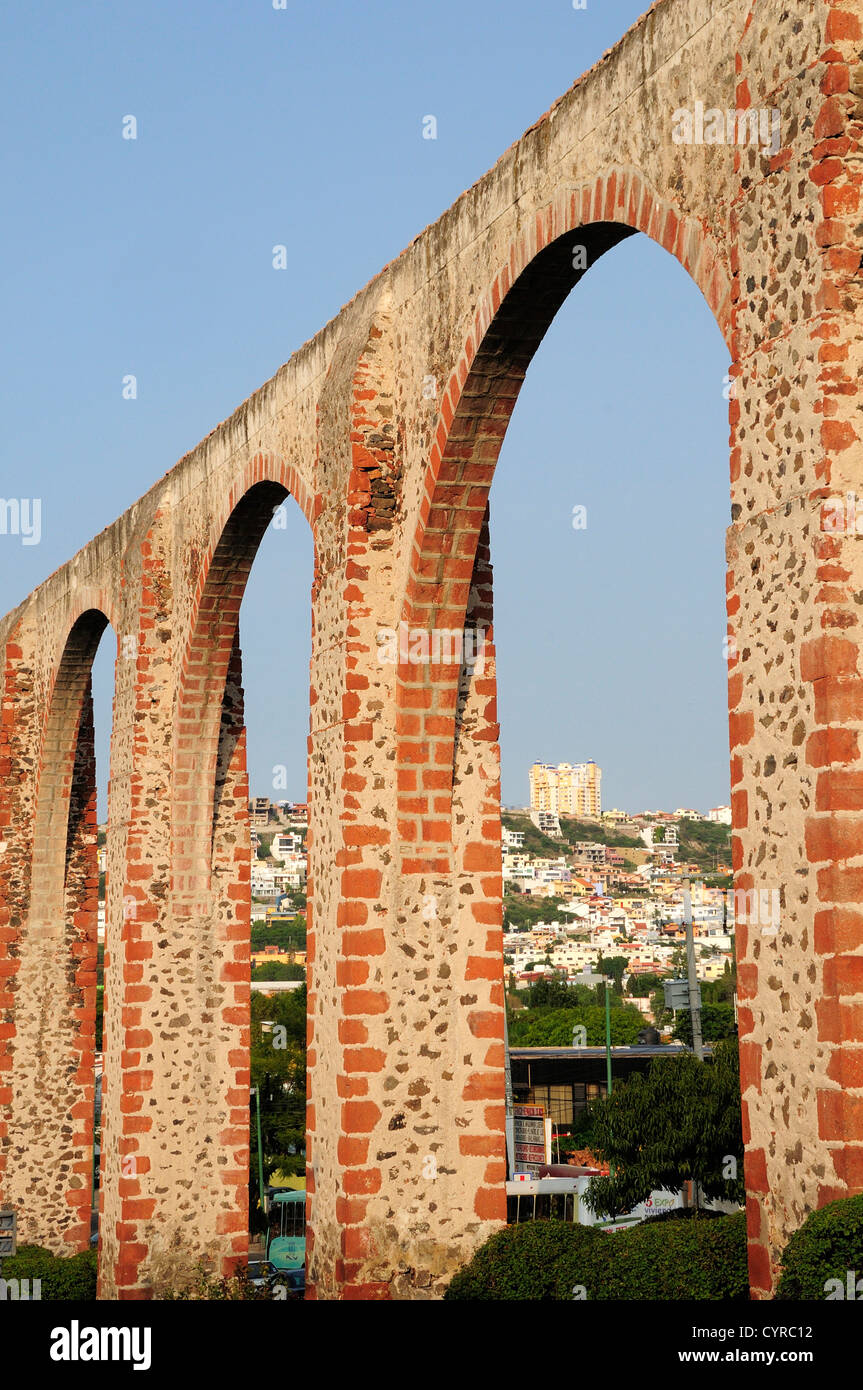 Messico, Bajio, Queretaro, Aquaduct archi che incorniciano vista verso gli edifici della città su una collina al di là. Foto Stock