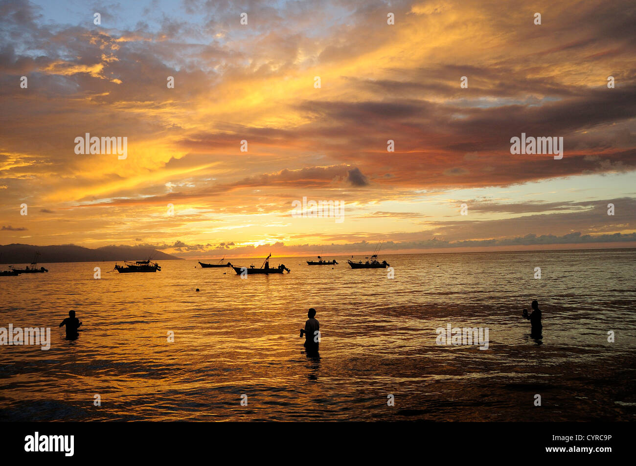 Messico, Jalisco, Puerto Vallarta, i pescatori in piedi in mare con barche per la pesca al largo al tramonto. Foto Stock