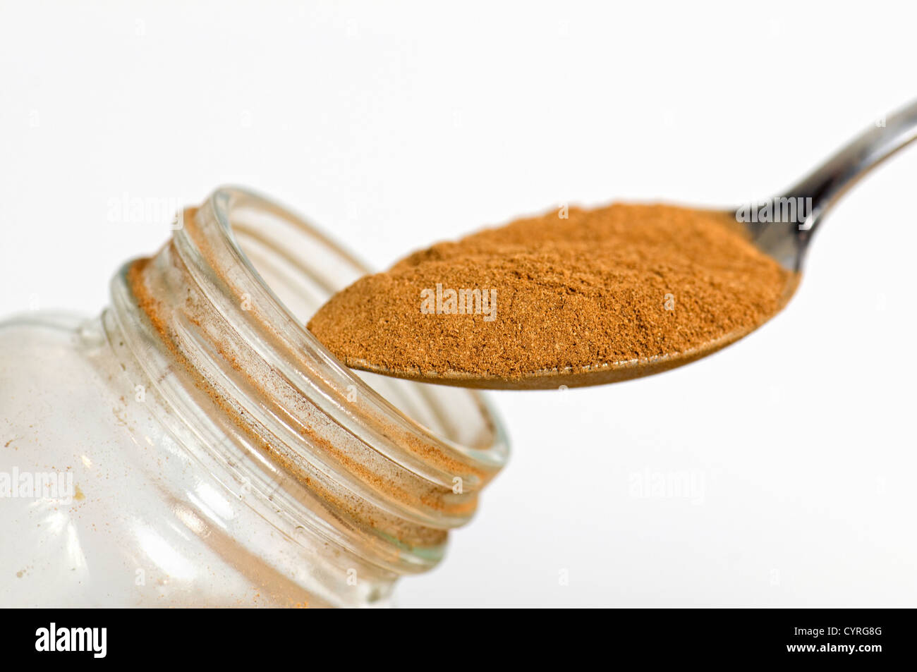 Close up di un cucchiaio di cannella in polvere contro uno sfondo bianco tenuto sopra un vaso aperto Foto Stock