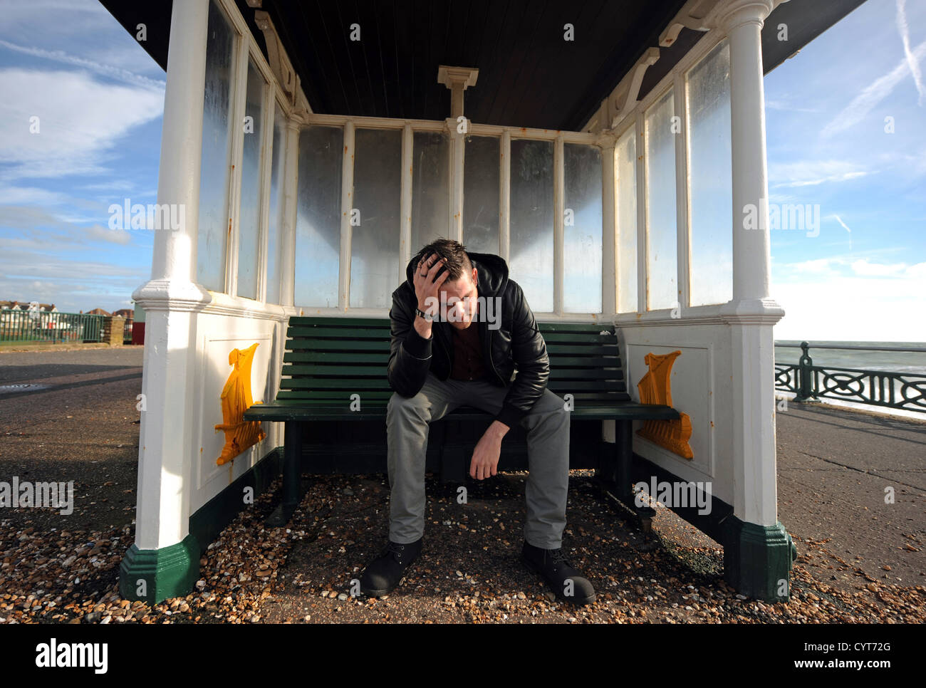 Giovane uomo lookiing e sentimento di disperazione e premuto seduto con la testa fra le mani in un rifugio sul lungomare Hove Regno Unito Foto Stock