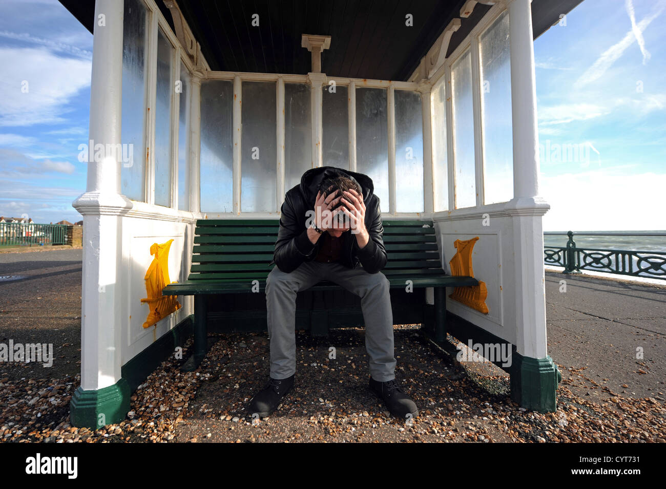 Giovane uomo lookiing e sentimento di disperazione e premuto seduto con la testa fra le mani in un rifugio sul lungomare Hove Regno Unito Foto Stock