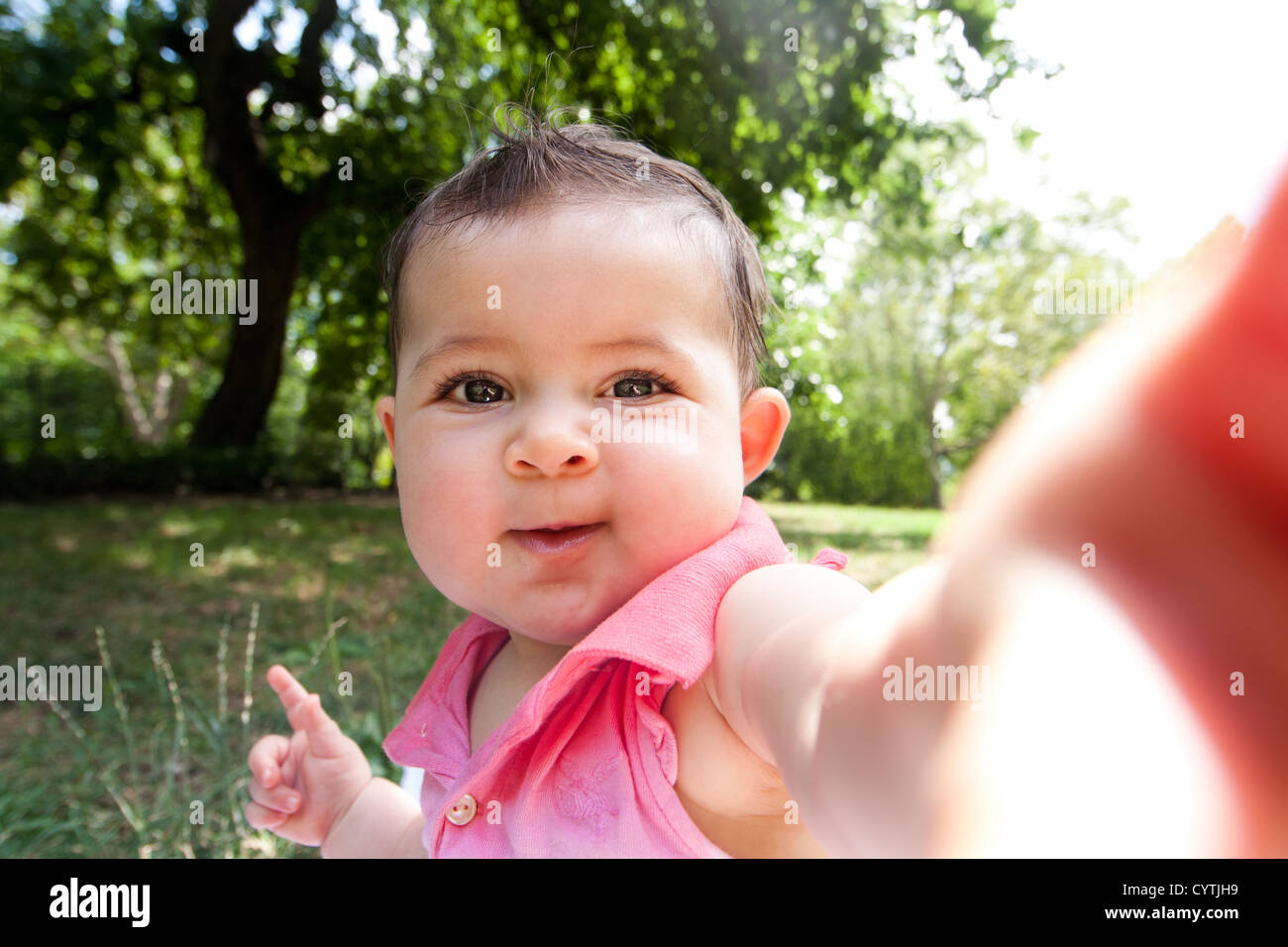 Carino divertente happy baby infant sticking braccio fuori come se sta prendendo autoritratto foto in un parco. Foto Stock