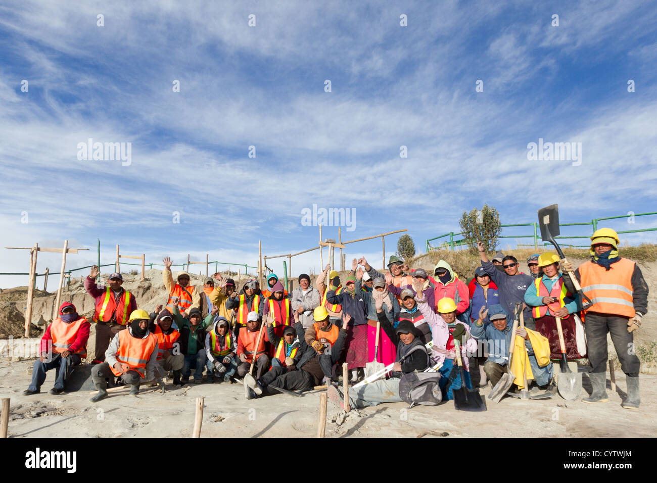 Un gruppo di operai edili, per lo più uomini, si radunano all'aperto in un luogo di lavoro, in posa per una foto di gruppo. Indossano indumenti di sicurezza, tra cui giubbotti arancioni ad alta visibilità, elmetti e alcuni Foto Stock