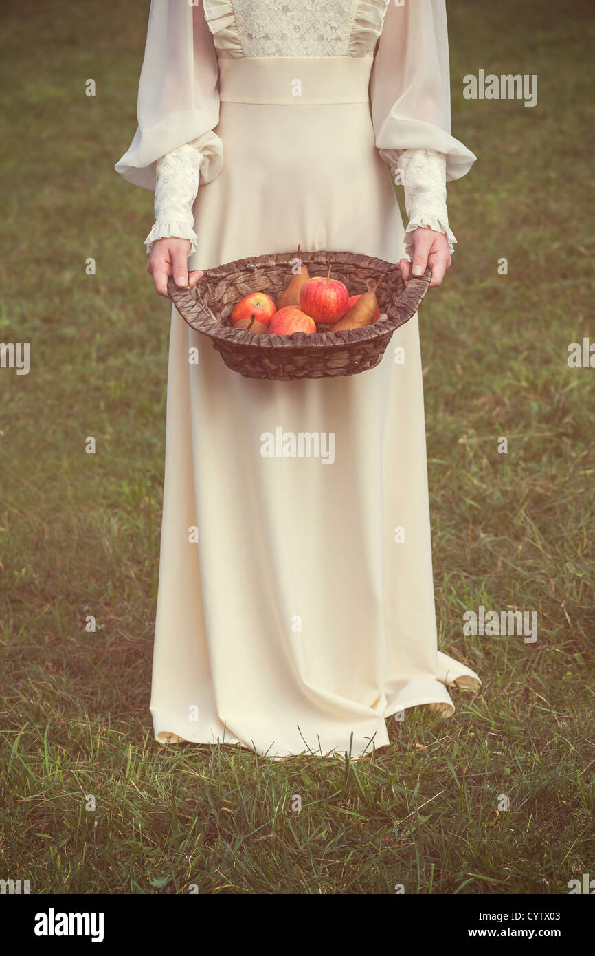 Una donna in un bianco edwardian vestito è in possesso di un cesto di frutta Foto Stock