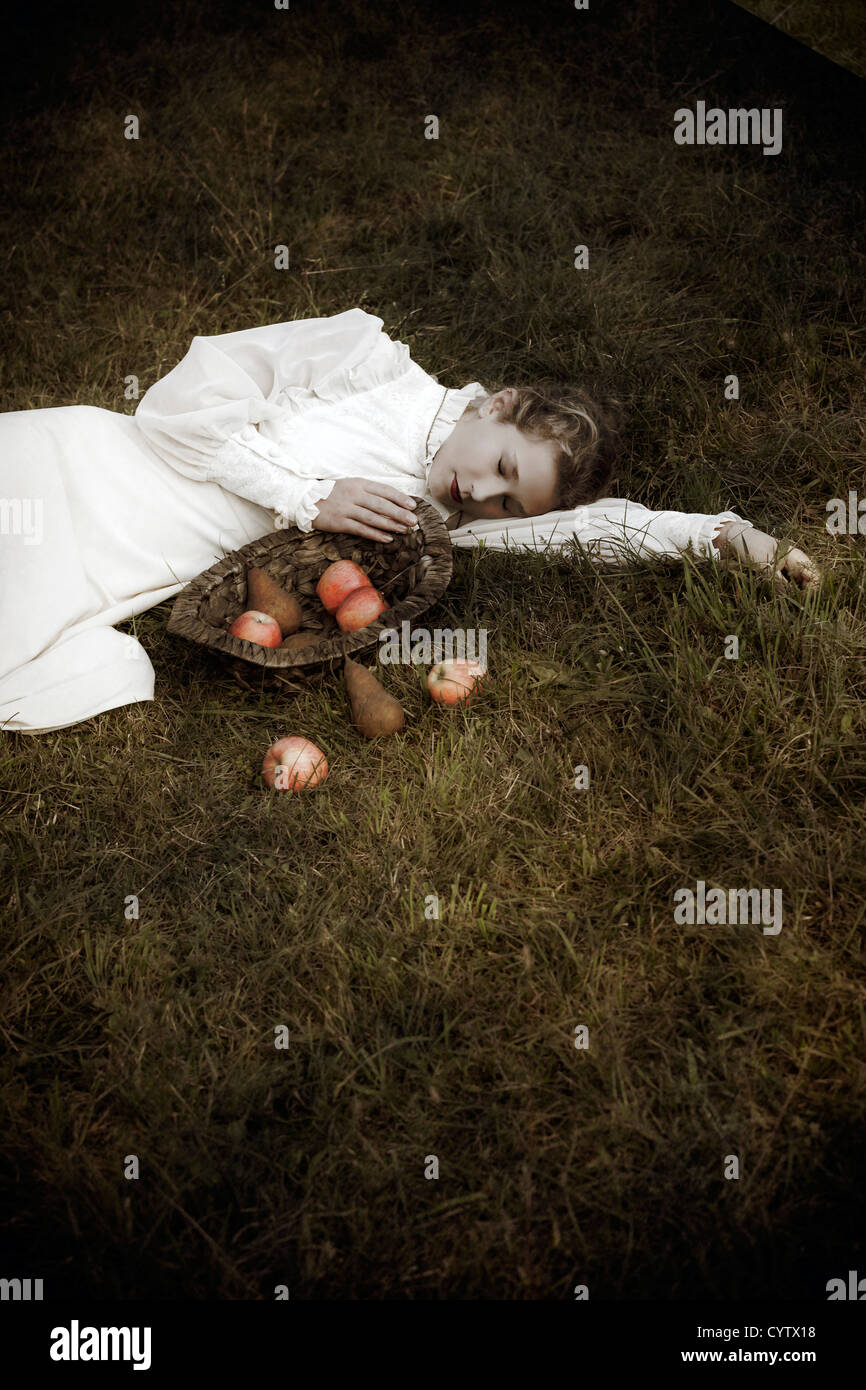Una donna in un bianco edwardian vestito è giacente in erba, di fronte a lei un cesto con frutta Foto Stock