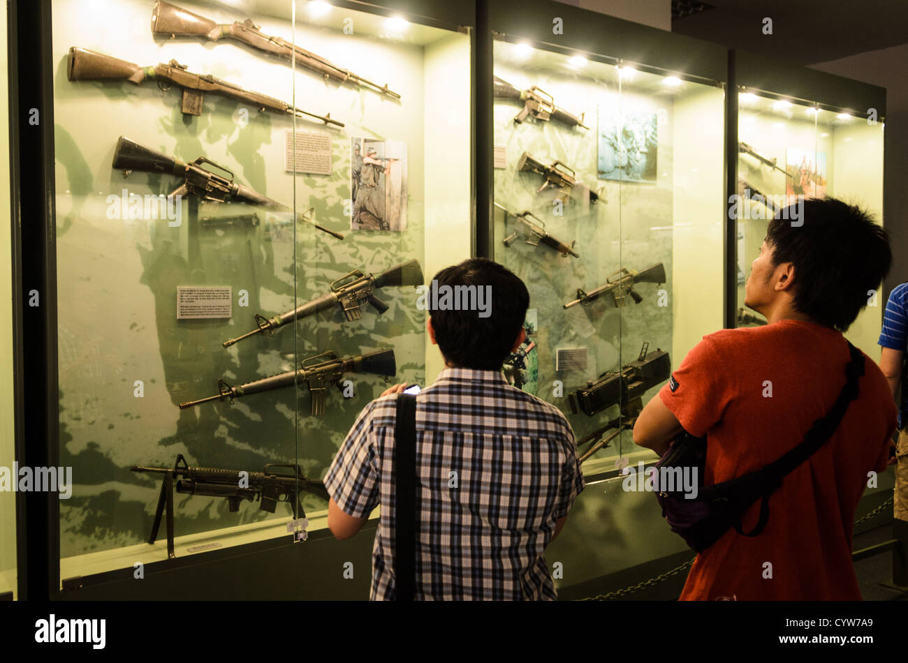 La città di HO CHI MINH, Vietnam - due visitatori guardano ad un involucro di vetro di alcune delle armi usate dagli Americani e sudvietnamiti forze durante la Guerra del Vietnam presso il Museo dei Resti della Guerra nella città di Ho Chi Minh (Saigon), Vietnam. Foto Stock