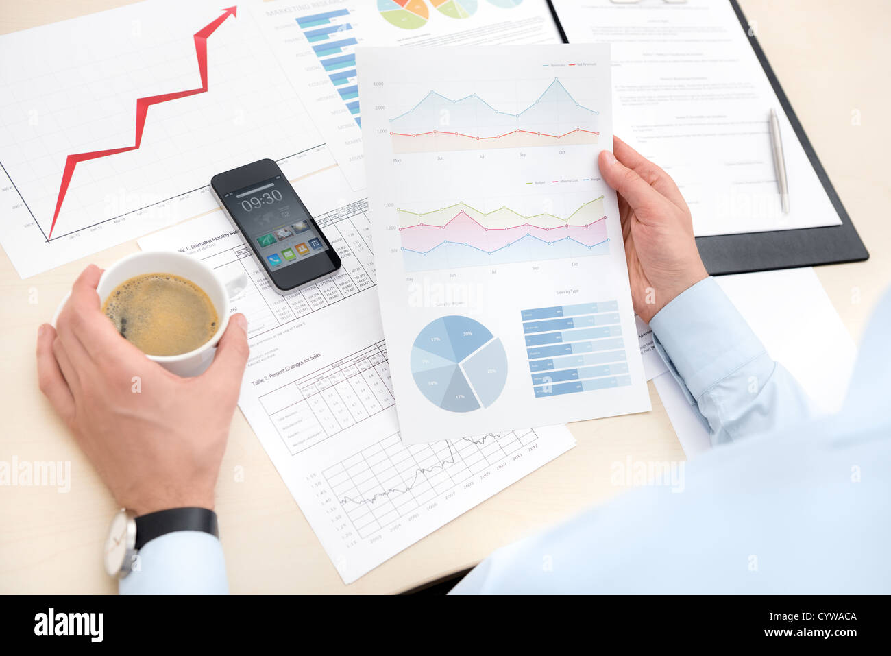 Imprenditore sul posto di lavoro bere il caffè e guardando alcune carte con i grafici e i numeri. Foto Stock