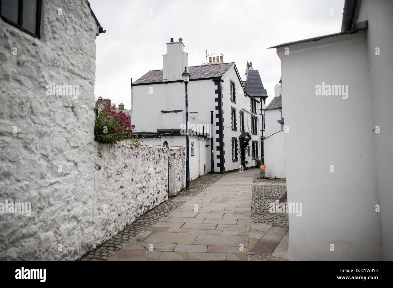 BEAUMARIS, Anglesey, Galles, un vicolo nella città di Beaumaris, caratterizzato da edifici bianchi con dettagli neri. La stretta strada è fiancheggiata da strutture tradizionali che riflettono il carattere architettonico di questa comunità di Anglesey. Beaumaris si trova sull'isola di Anglesey al largo della costa settentrionale del Galles. La città è ampiamente conosciuta per il suo castello medievale, costruito alla fine del XIII secolo come parte della conquista del Galles da parte di Edoardo i. L'insediamento si sviluppò intorno al castello e conserva gran parte della sua struttura storica delle strade. Beaumaris è una destinazione popolare per i visitatori che esplorano Ang Foto Stock