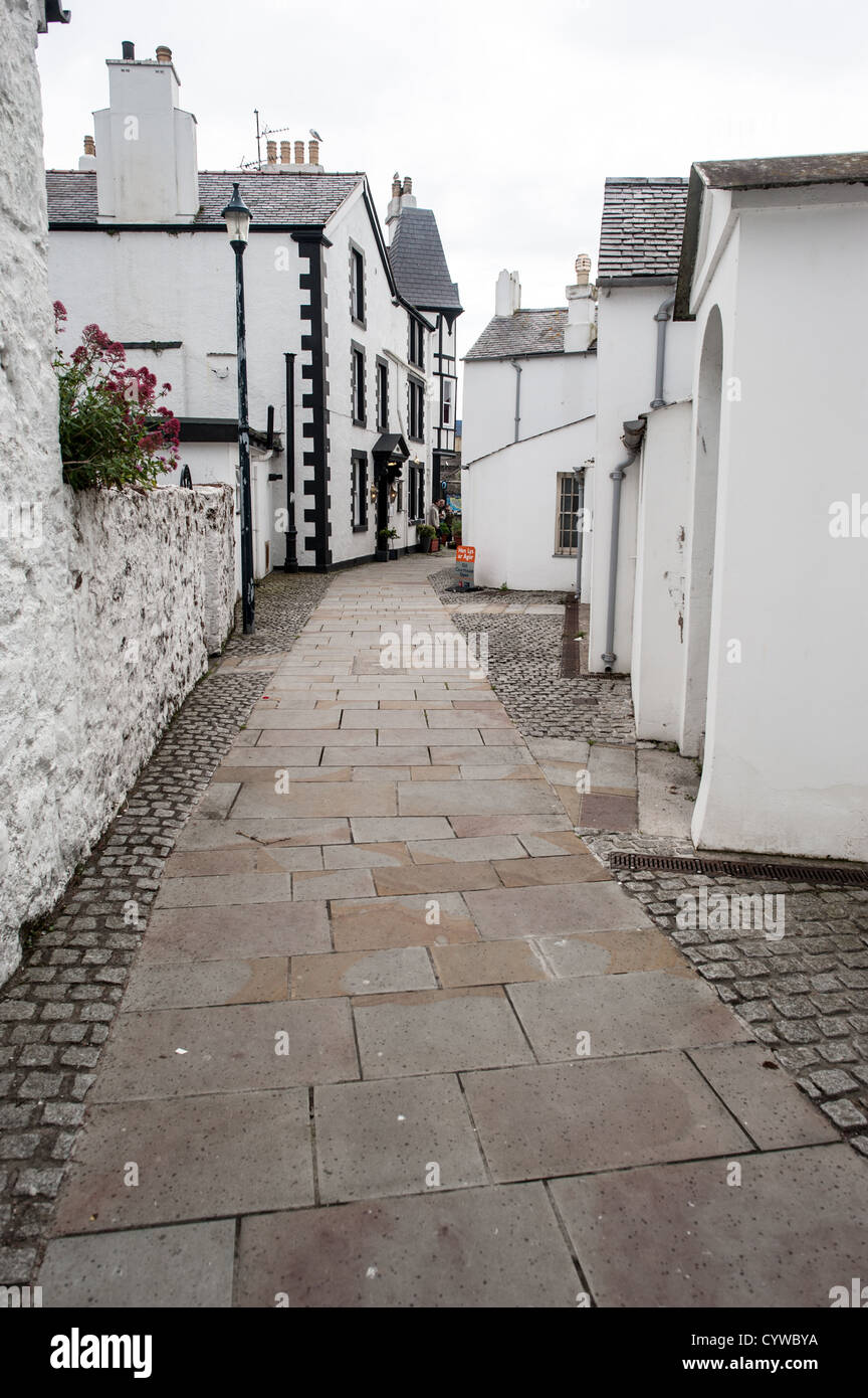 BEAUMARIS, Anglesey, Galles, un vicolo nella città di Beaumaris, caratterizzato da edifici bianchi con dettagli neri. La stretta strada è fiancheggiata da strutture tradizionali che riflettono il carattere architettonico di questa comunità di Anglesey. Beaumaris si trova sull'isola di Anglesey al largo della costa settentrionale del Galles. La città è ampiamente conosciuta per il suo castello medievale, costruito alla fine del XIII secolo come parte della conquista del Galles da parte di Edoardo i. L'insediamento si sviluppò intorno al castello e conserva gran parte della sua struttura storica delle strade. Beaumaris è una destinazione popolare per i visitatori che esplorano Ang Foto Stock