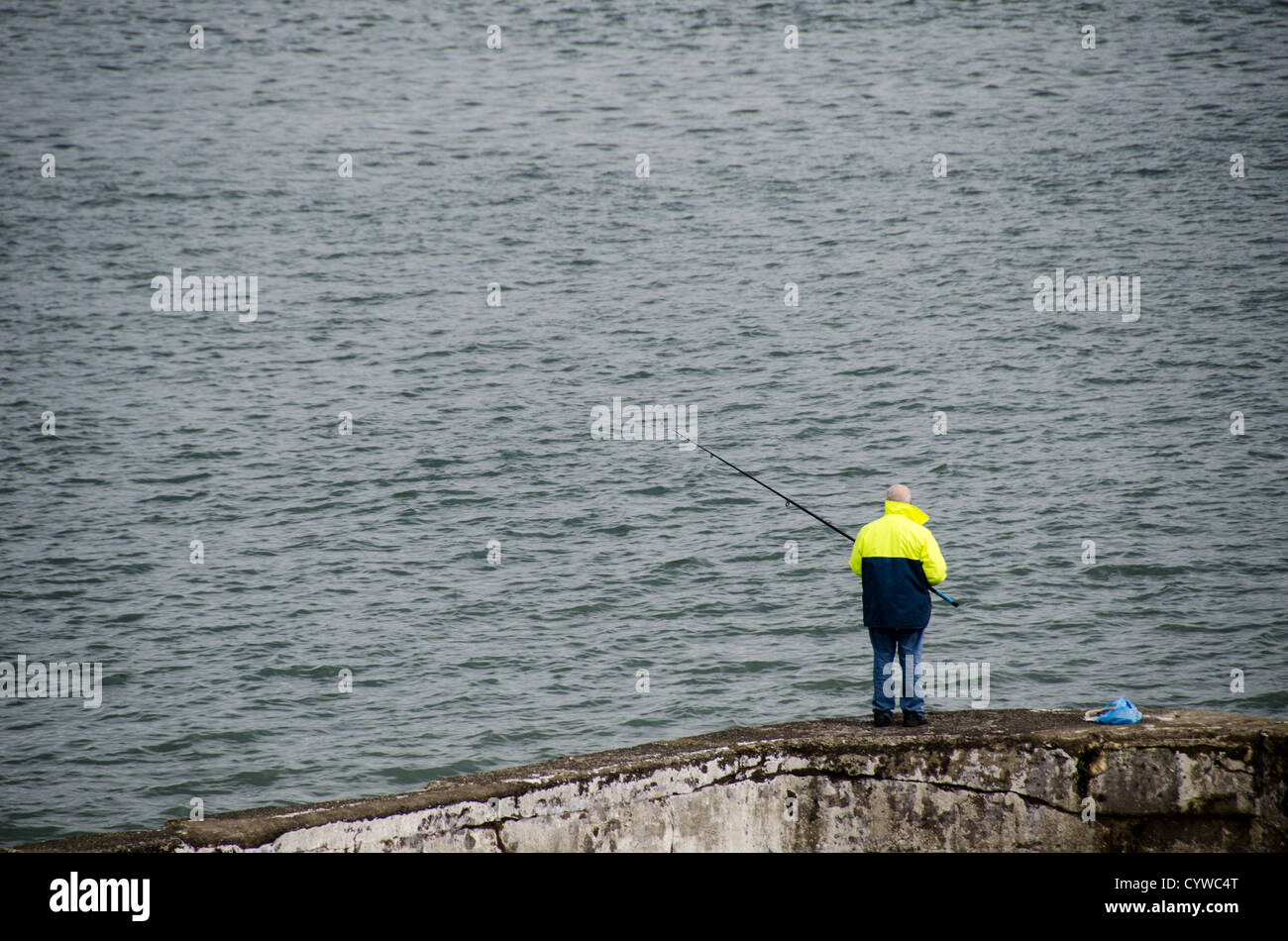 BEAUMARIS, Galles - Un pescatore solitario getta la sua linea da un vecchio muro di pietra lungo il lungomare di Beaumaris sull'isola di Anglesey. La tranquilla scena cattura l'intramontabile fascino del mare sullo sfondo dello stretto di Menai, con le montagne di Snowdonia visibili in lontananza. Questa immagine racchiude il fascino tranquillo e la bellezza naturale che attirano sia pescatori che turisti in questa pittoresca cittadina costiera gallese. Foto Stock