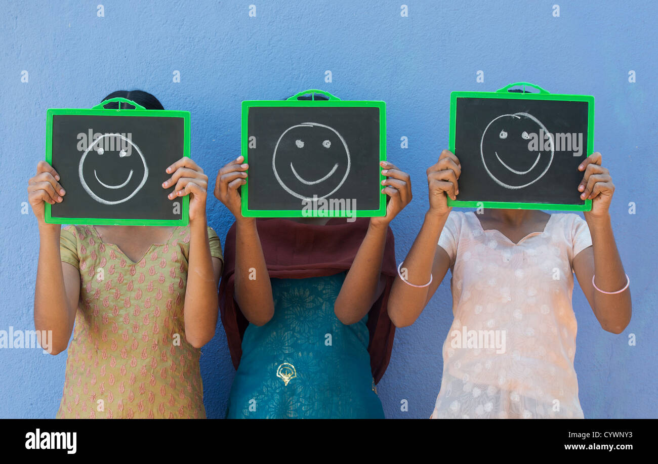 Tre villaggio indiano ragazze con HAPPY SMILE disegnato su lavagne che coprono i loro volti. India Foto Stock