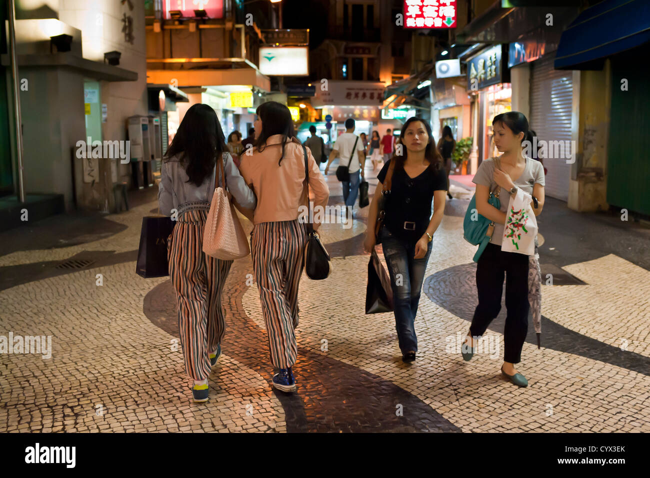 Due donne in pantaloni di adattamento a piedi a braccetto a Macau. Foto Stock