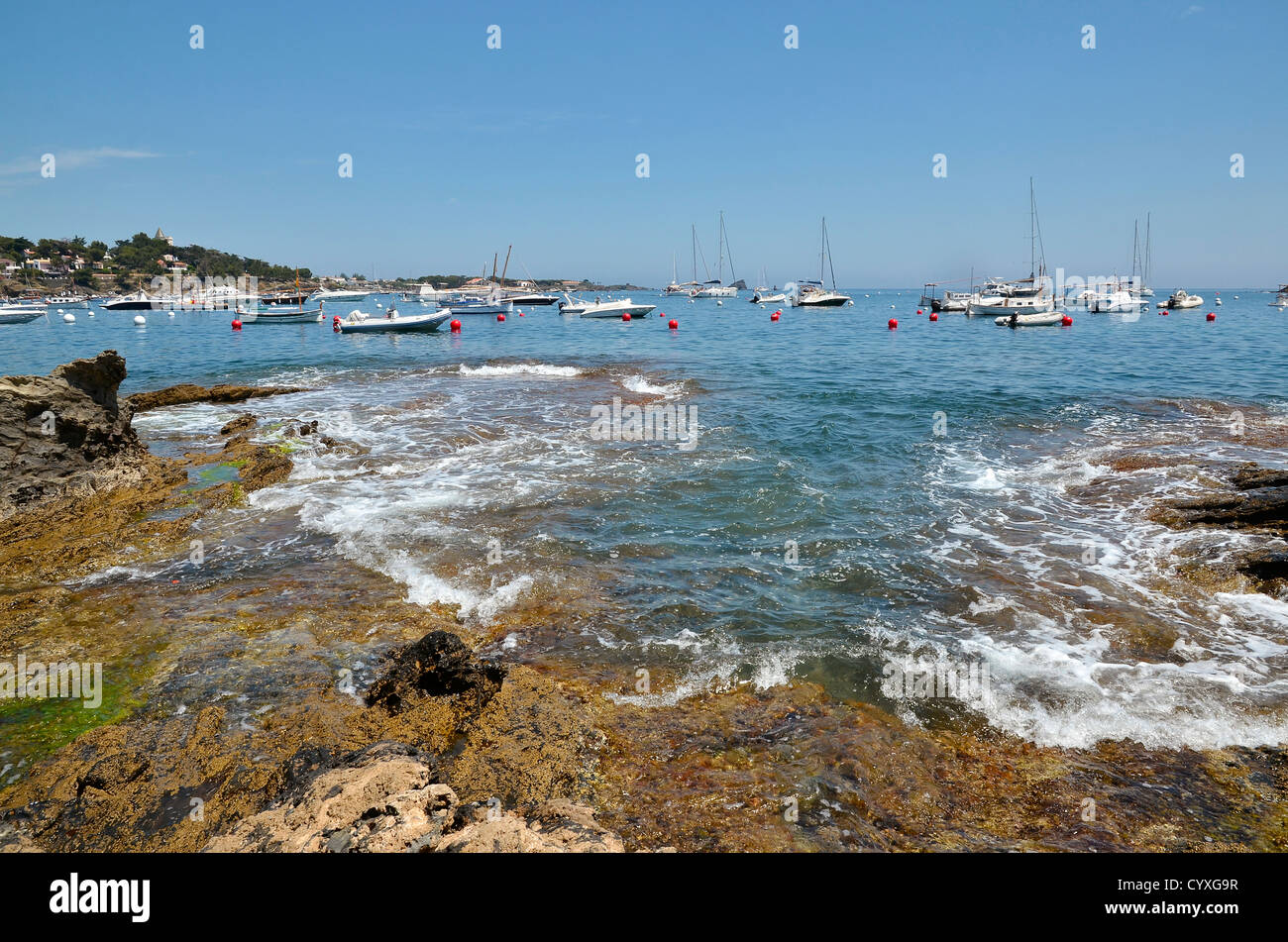 Costa rocciosa con onde e barche a Cadaqués, comune sulla Costa Brava a nord-est la Catalogna in Spagna Foto Stock
