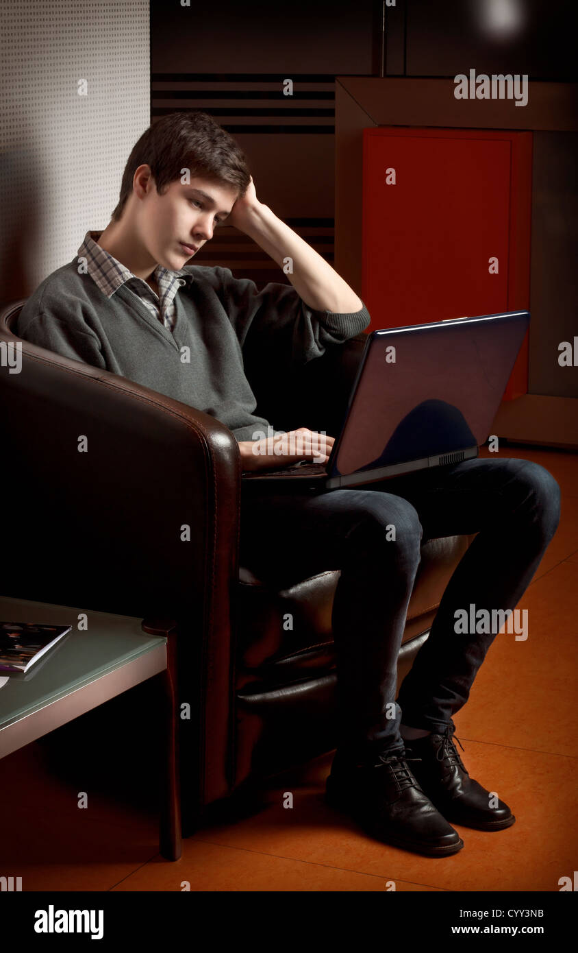 Giovane ragazzo cerca riflessivo sul laptop Foto Stock