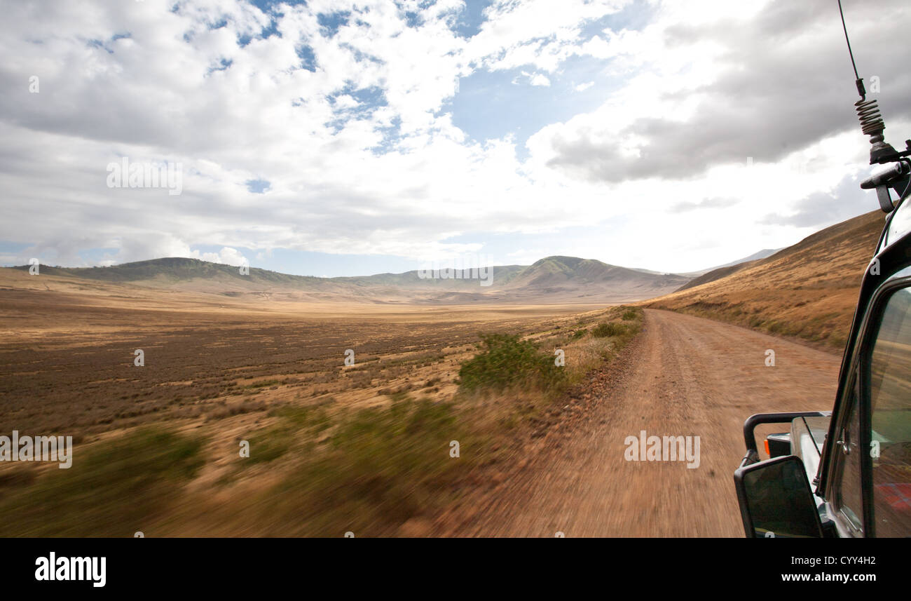 Il modulo visualizza la finestra di Safari di un veicolo come esso trascina verso il basso la strada verso una gamma di montagna. Tanzania Foto Stock