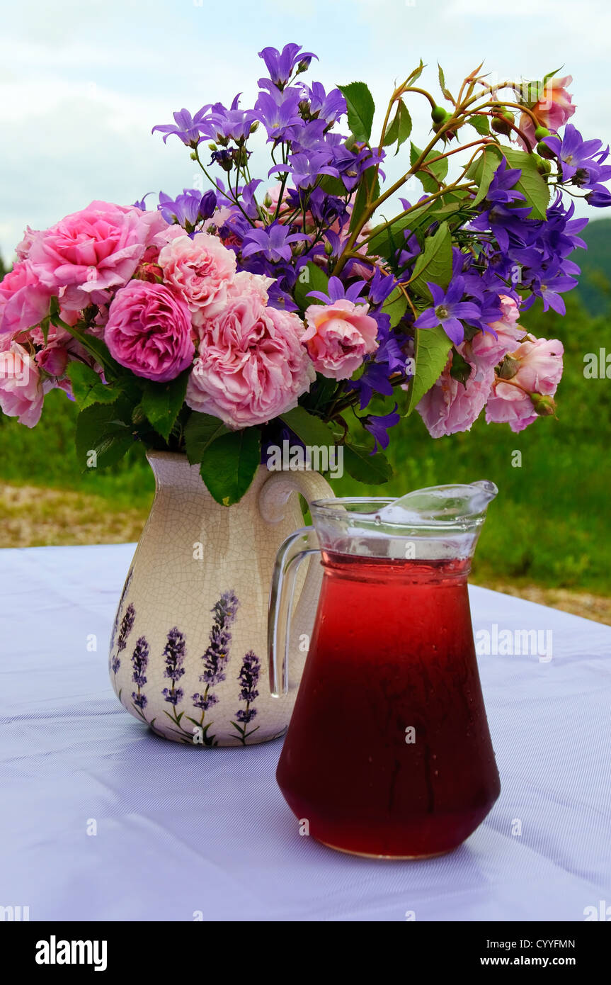 Un mazzo di fiori e una tazza con succo rosso fuori in giardino Foto Stock