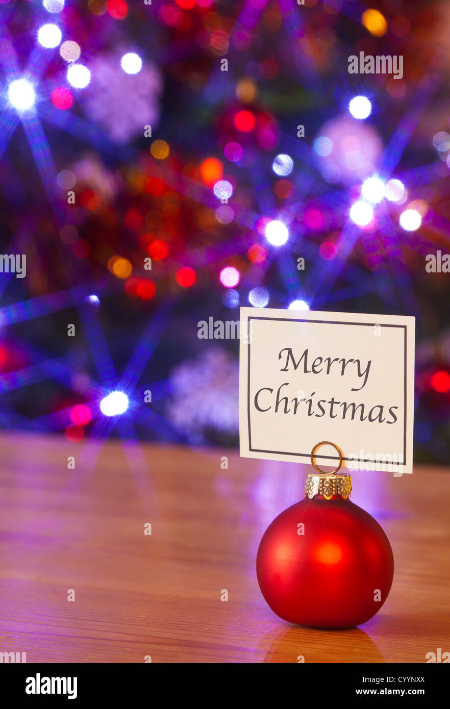 Una pallina rossa segnaposto con una scheda che dice Buon Natale e le luci fairy sfocato sull'albero di Natale dietro. Foto Stock