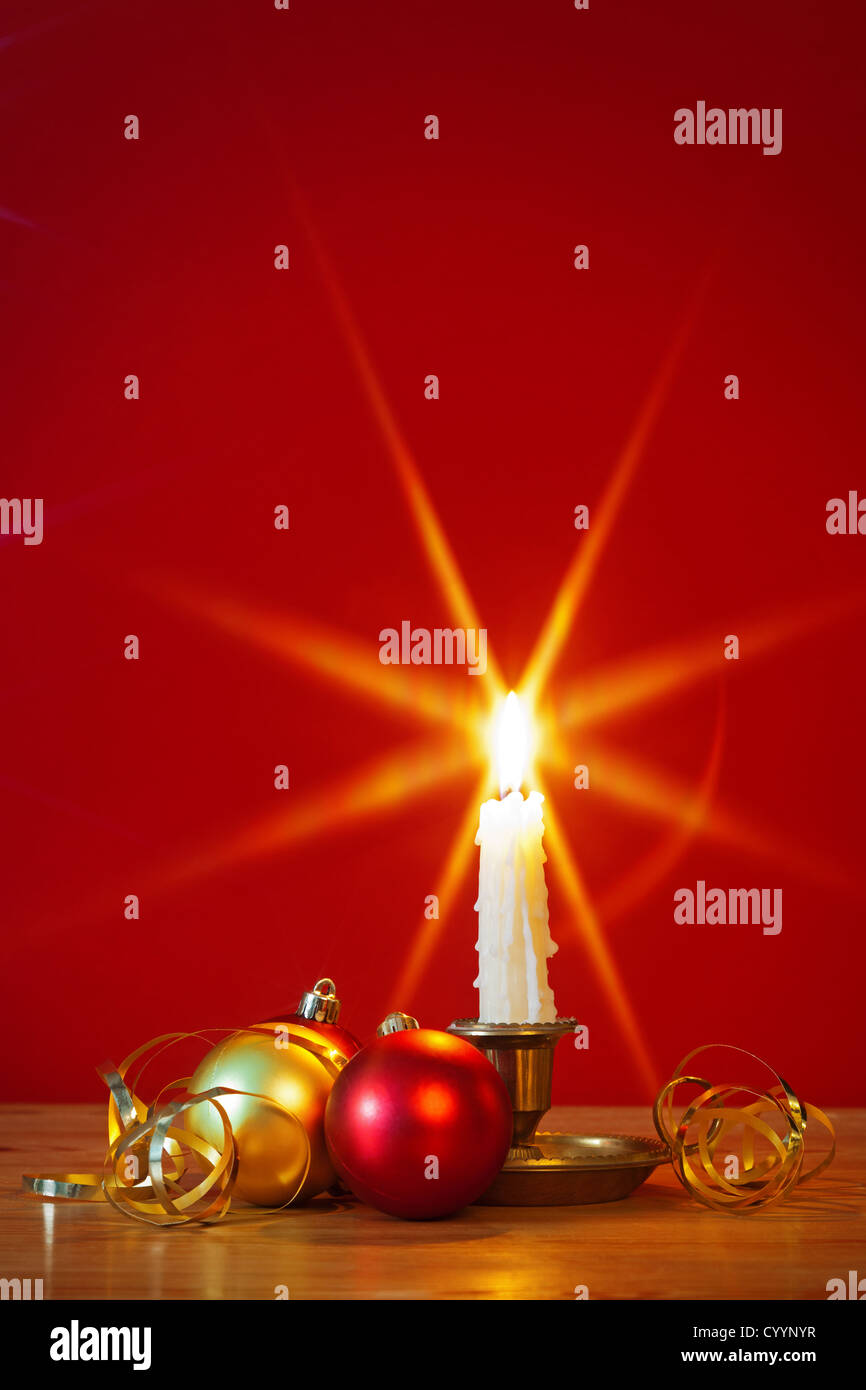 Una candela accesa nel supporto in ottone con decorazioni natalizie e sfondo rosso, stella filtro utilizzato durante l'acquisizione per la fiamma Foto Stock