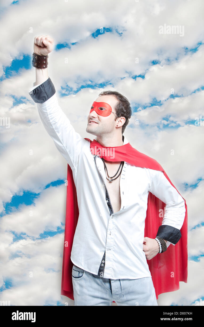 Giovane uomo in costume da supereroe con la mano alzata contro il cielo nuvoloso Foto Stock
