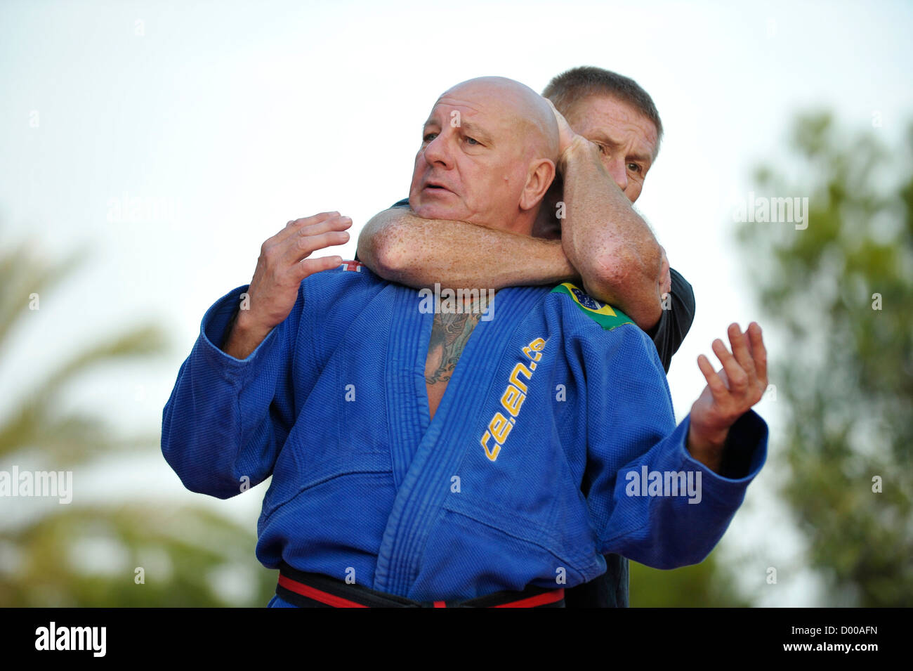 Maschio di arti marziali studente nel suo degli anni quaranta ha il suo insegnante negli anni cinquanta in una headlock nel parco con palme Foto Stock