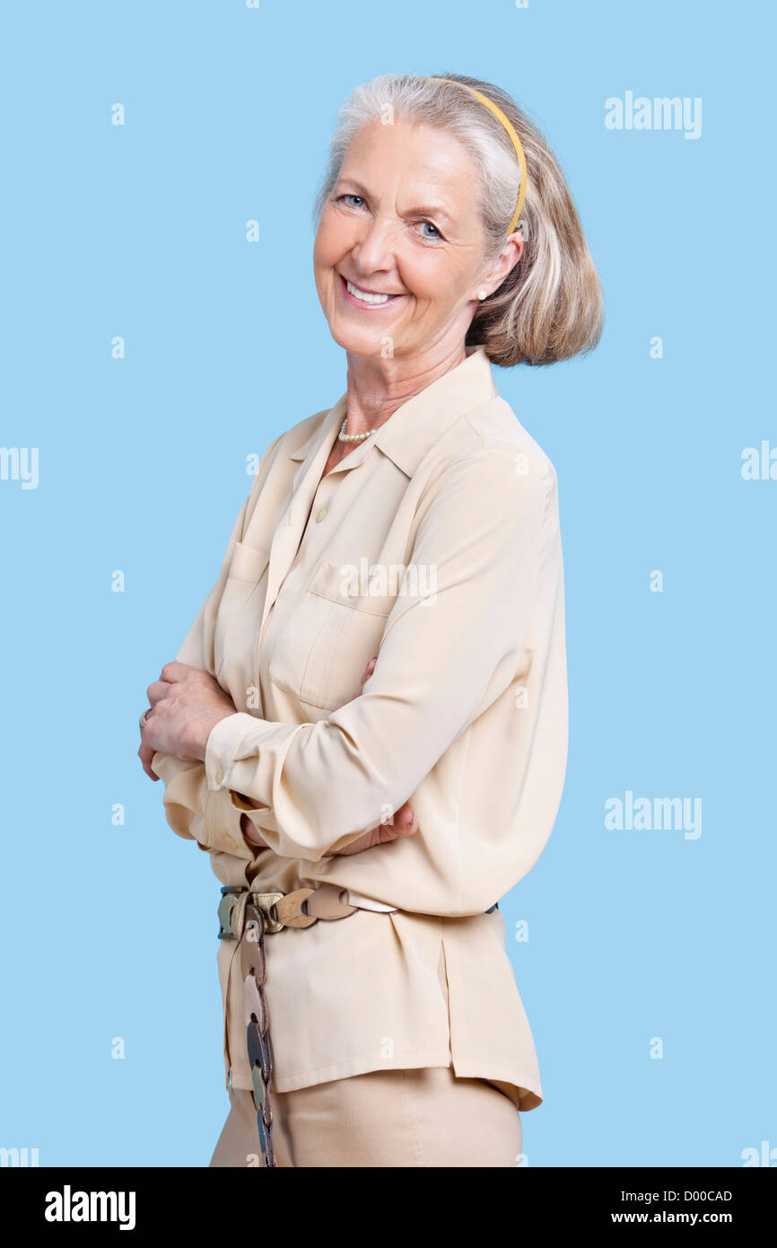Ritratto di sorridente donna senior in casuals con le braccia incrociate contro sfondo blu Foto Stock