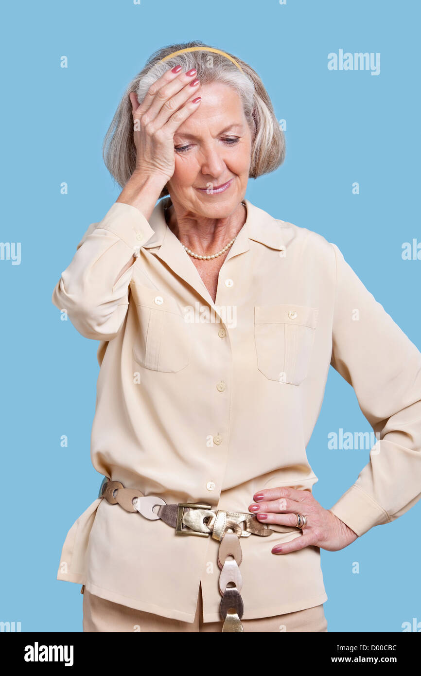Senior donna in casuals soffrono di mal di testa contro sfondo blu Foto Stock