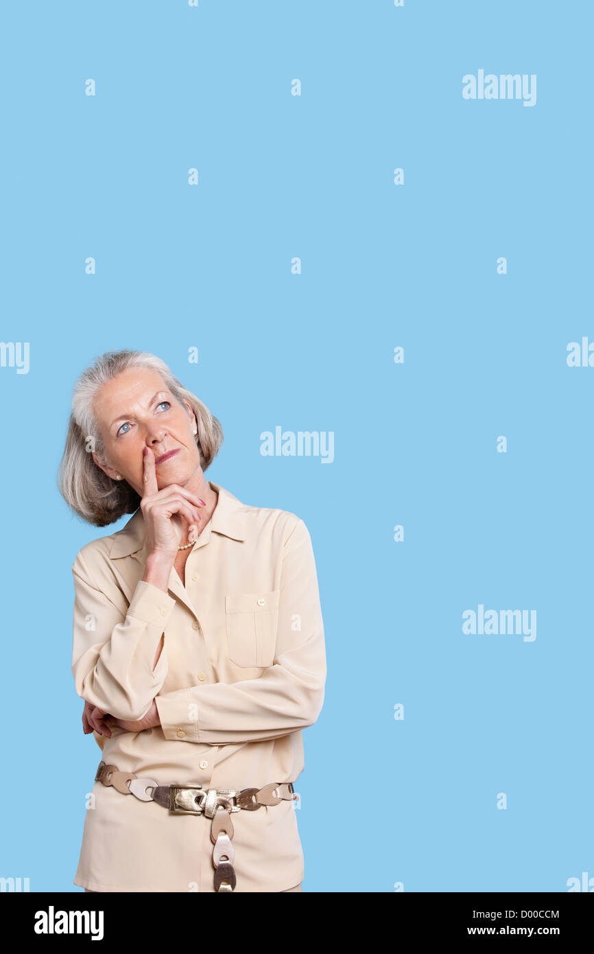 Contemplativa donna senior in casuals con mano sul mento contro sfondo blu Foto Stock