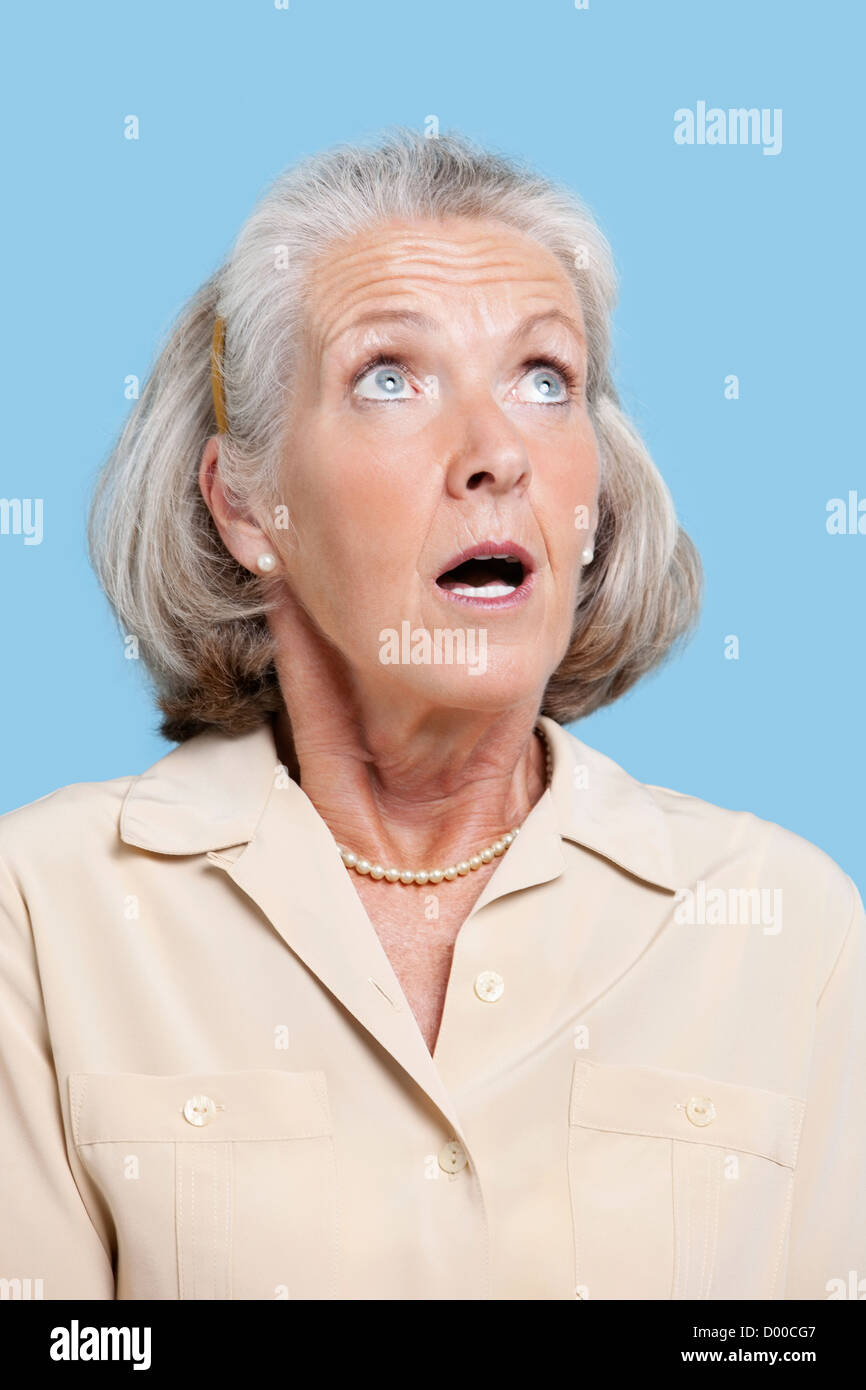 Scioccato senior donna in casuals guardando lontano contro lo sfondo blu Foto Stock