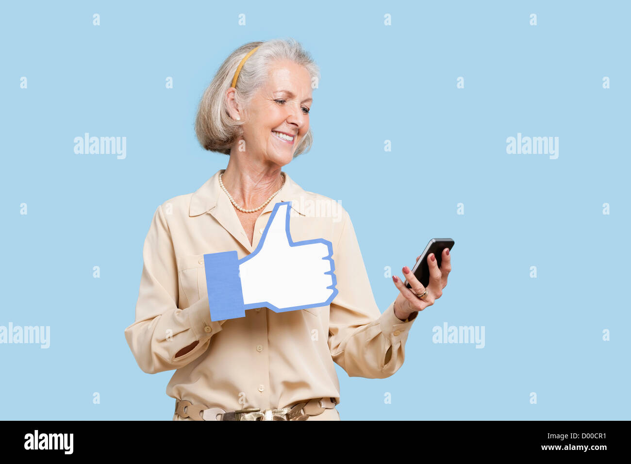 Donna senior con un telefono cellulare holding fake like button contro sfondo blu Foto Stock