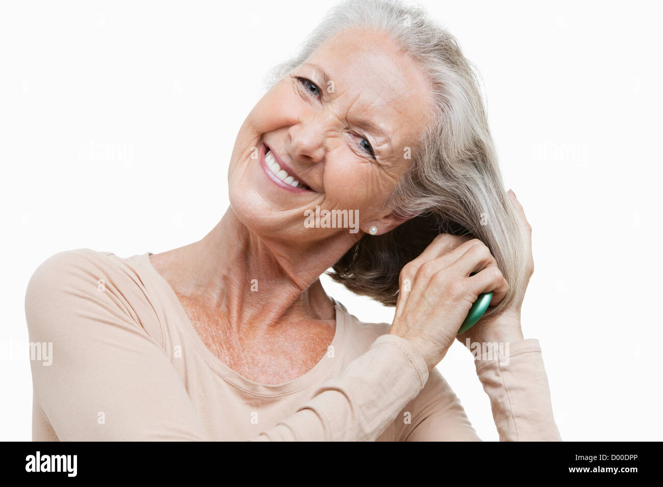 Ritratto di sorridente donna senior pettinare i capelli contro uno sfondo bianco Foto Stock