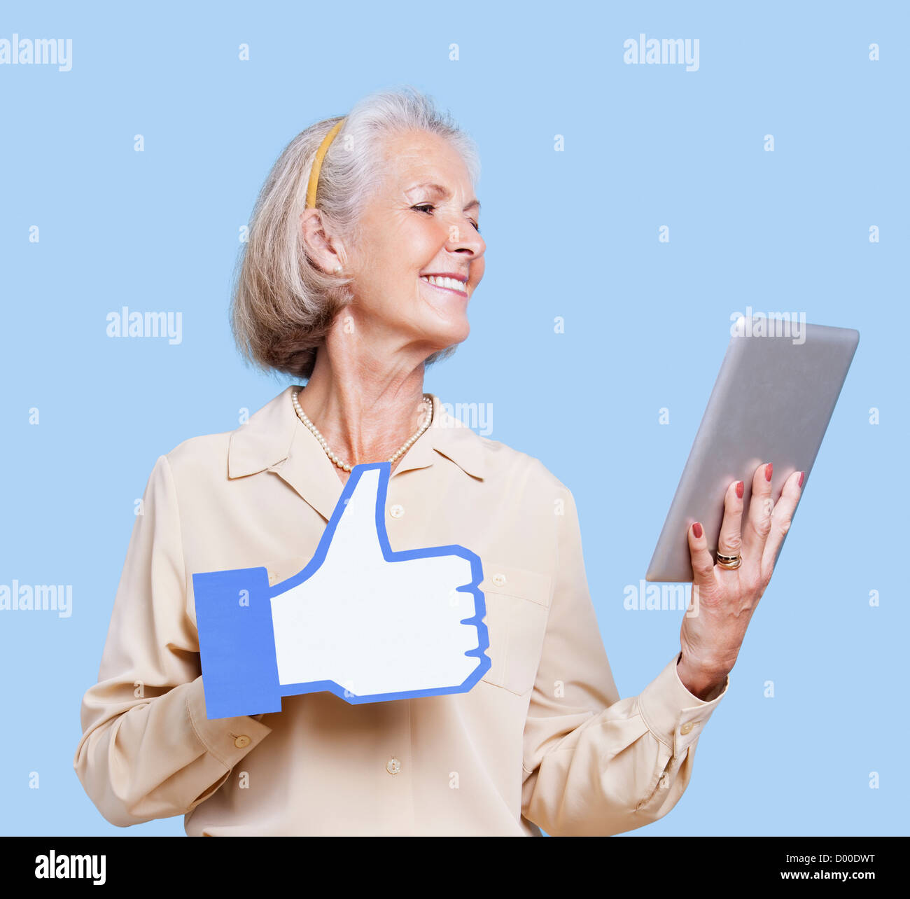 Senior donna con tablet PC azienda fake like button contro sfondo blu Foto Stock