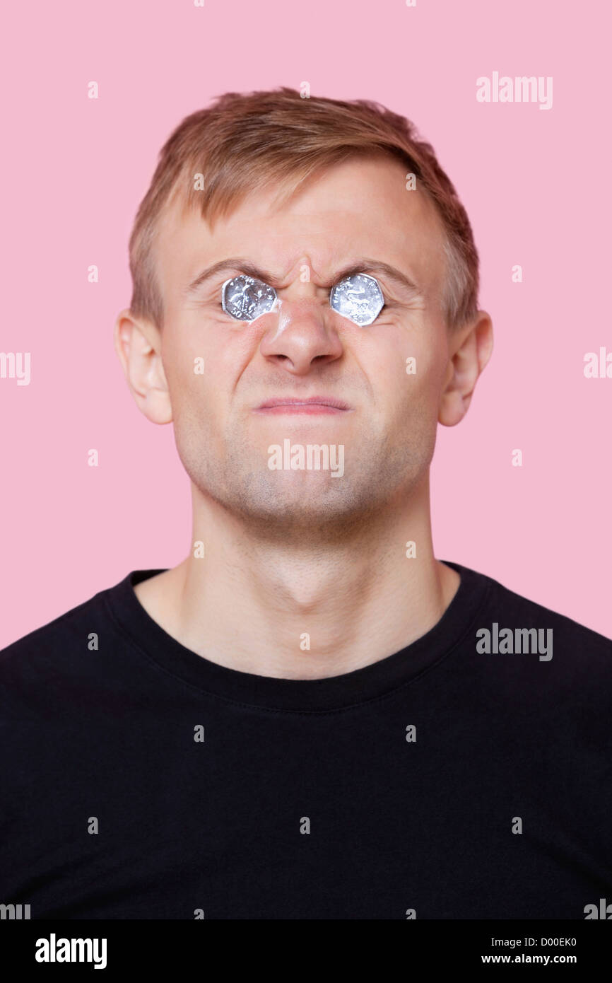 Funny giovane uomo che copre gli occhi con le monete su sfondo rosa Foto Stock