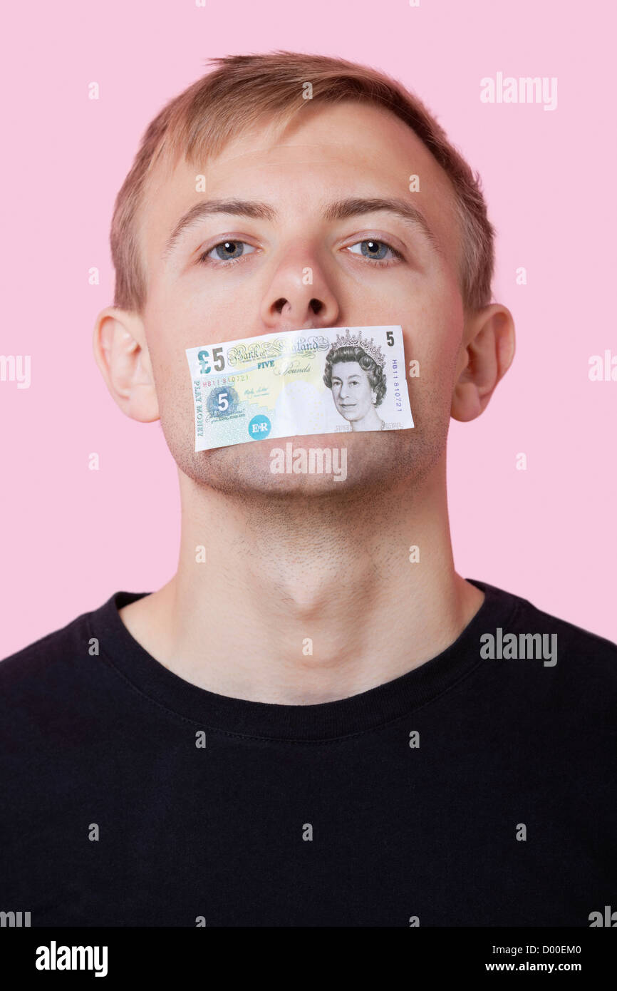 Ritratto di un giovane uomo con la carta moneta bloccata sulla sua bocca contro sfondo rosa Foto Stock