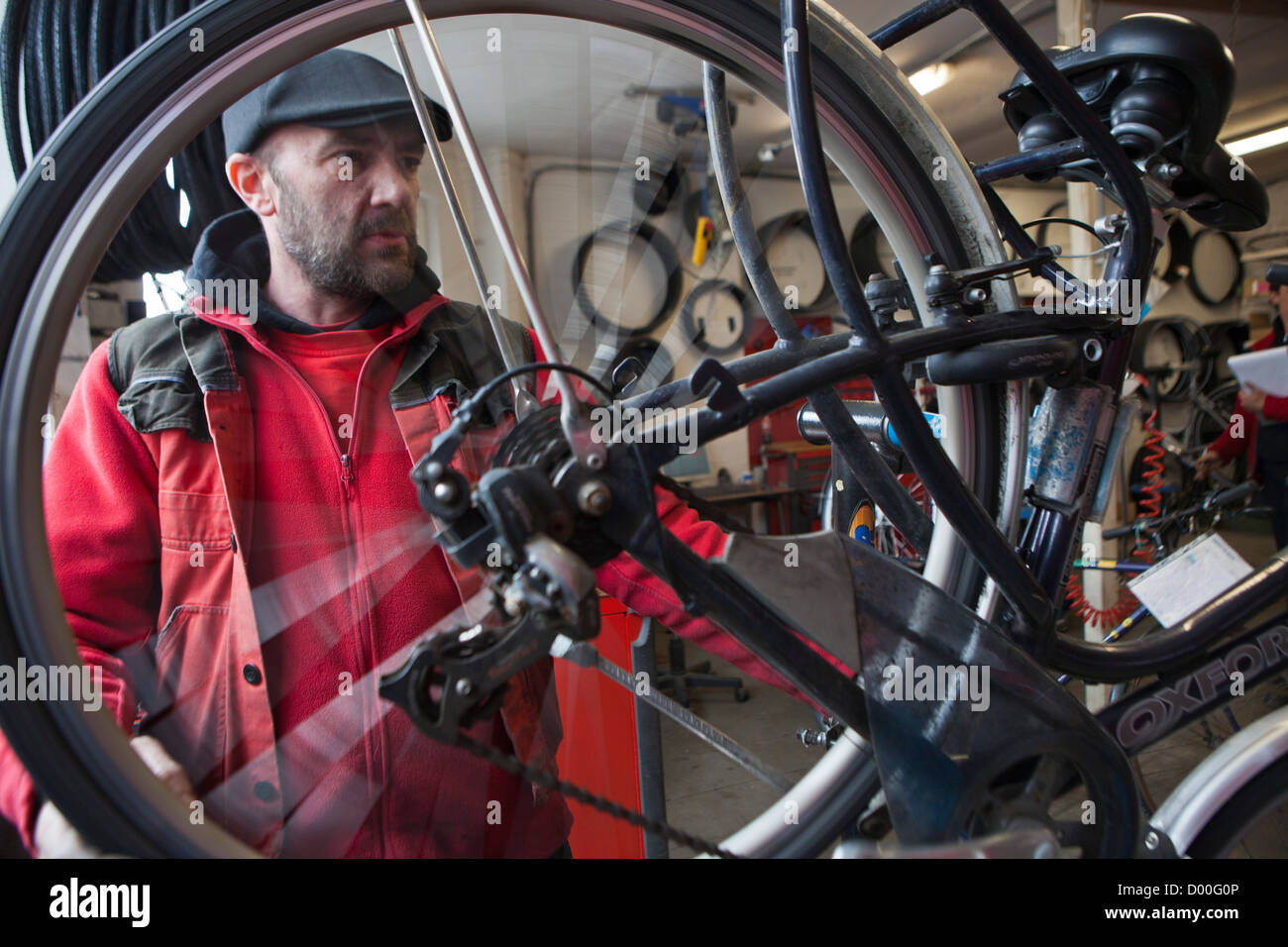 Un ciclo repairman controlla la rotazione di una ruota in un workshop in bicicletta. Ghent, Belgio. Foto Stock