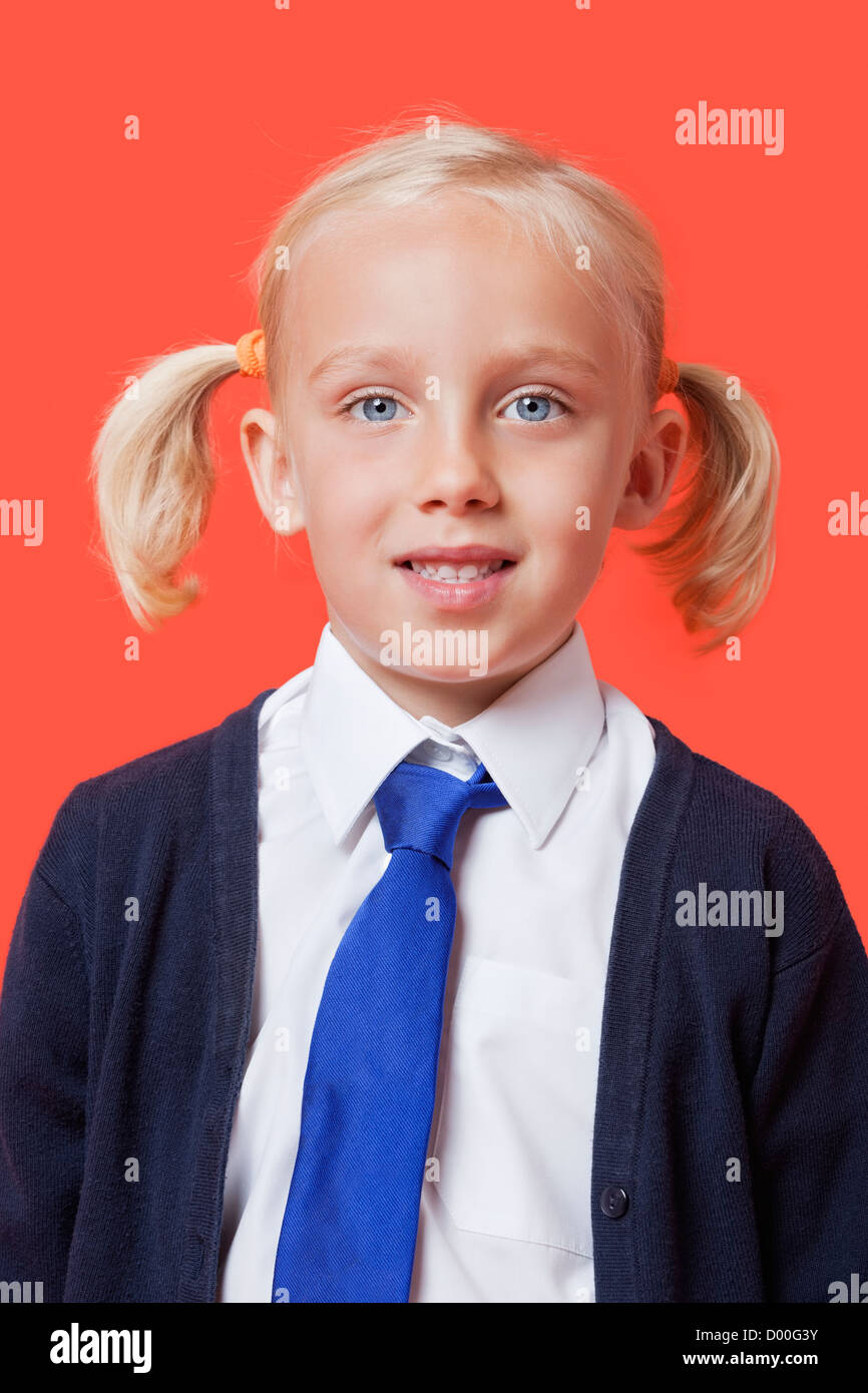 Ritratto di un felice schoolgirl in uniforme su sfondo arancione Foto Stock