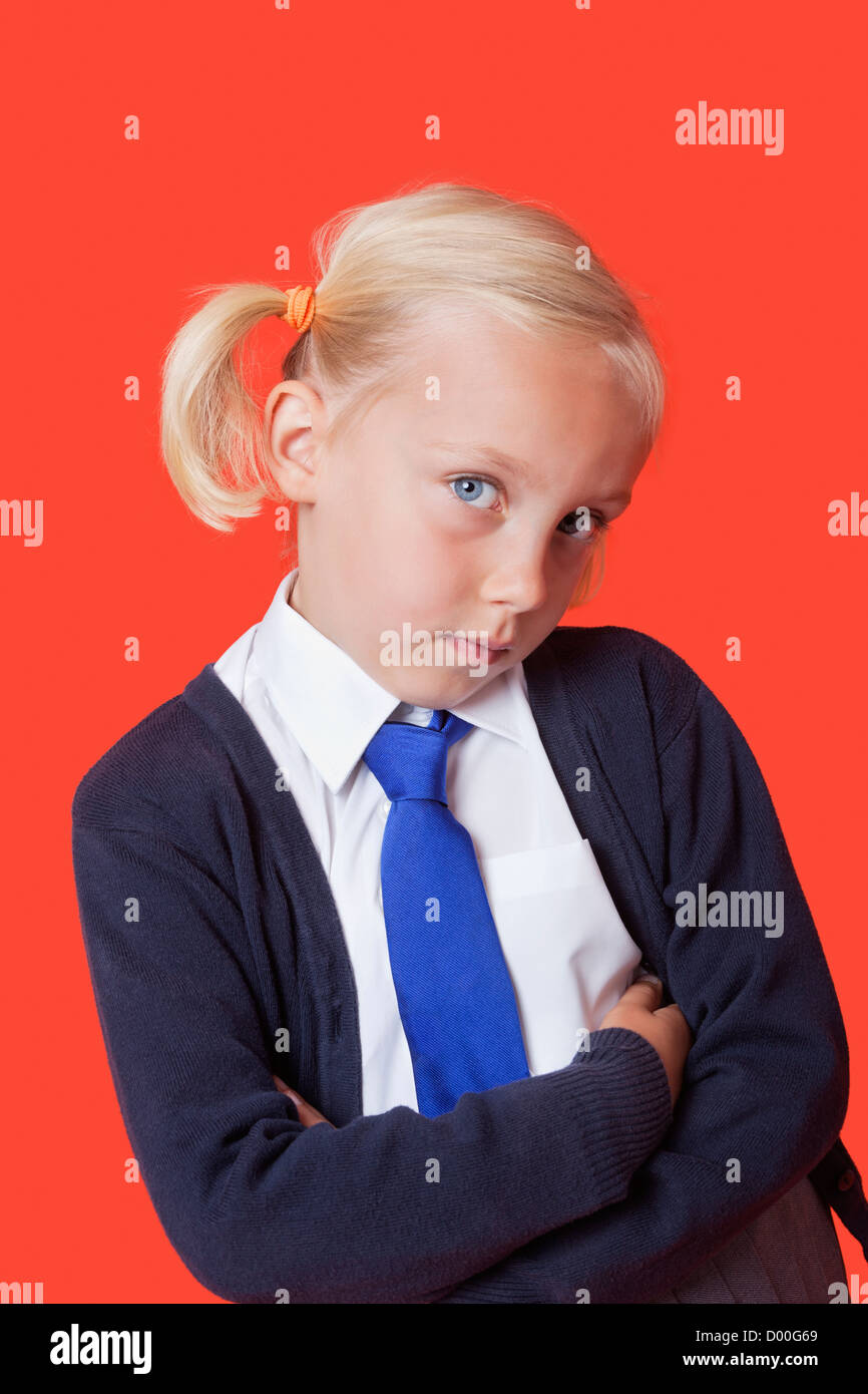 Ritratto di un giovane schoolgirl con le braccia incrociate su sfondo arancione Foto Stock