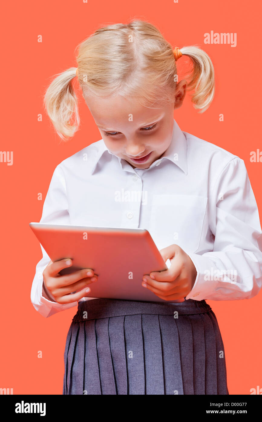 Felice giovani schoolgirl utilizzando tablet PC su sfondo arancione Foto Stock