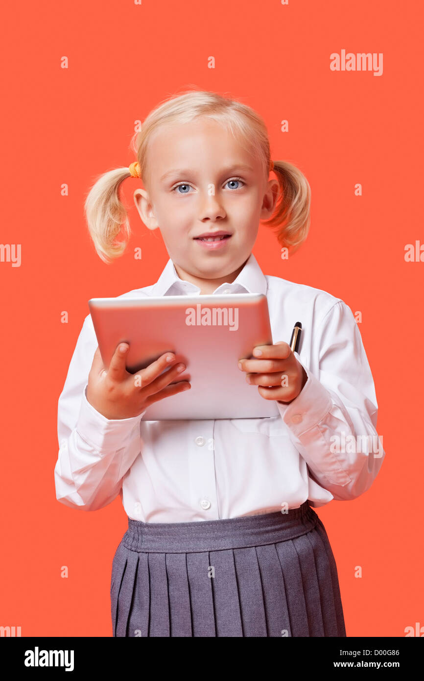 Ritratto di un giovane felice schoolgirl holding tablet PC su sfondo arancione Foto Stock