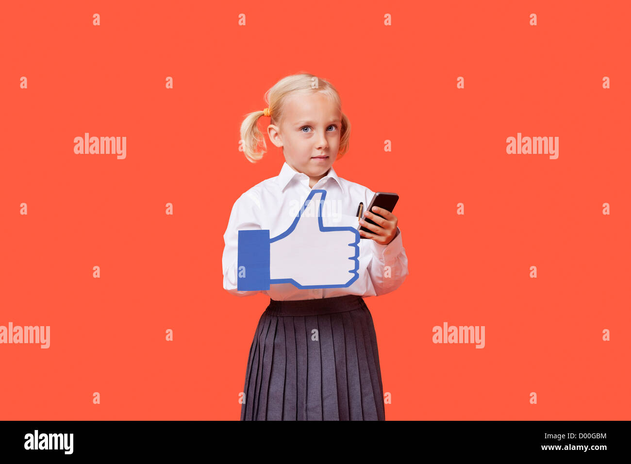 Ritratto di un giovane schoolgirl con telefono cellulare holding fake come pulsante sopra lo sfondo arancione Foto Stock