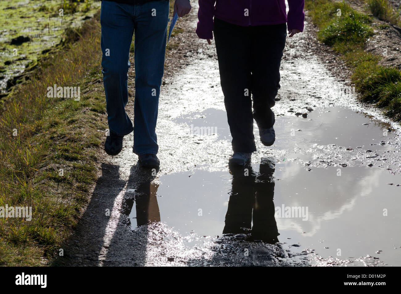 Gambe di due persone a piedi attraverso pozzanghere su un sentiero Foto Stock